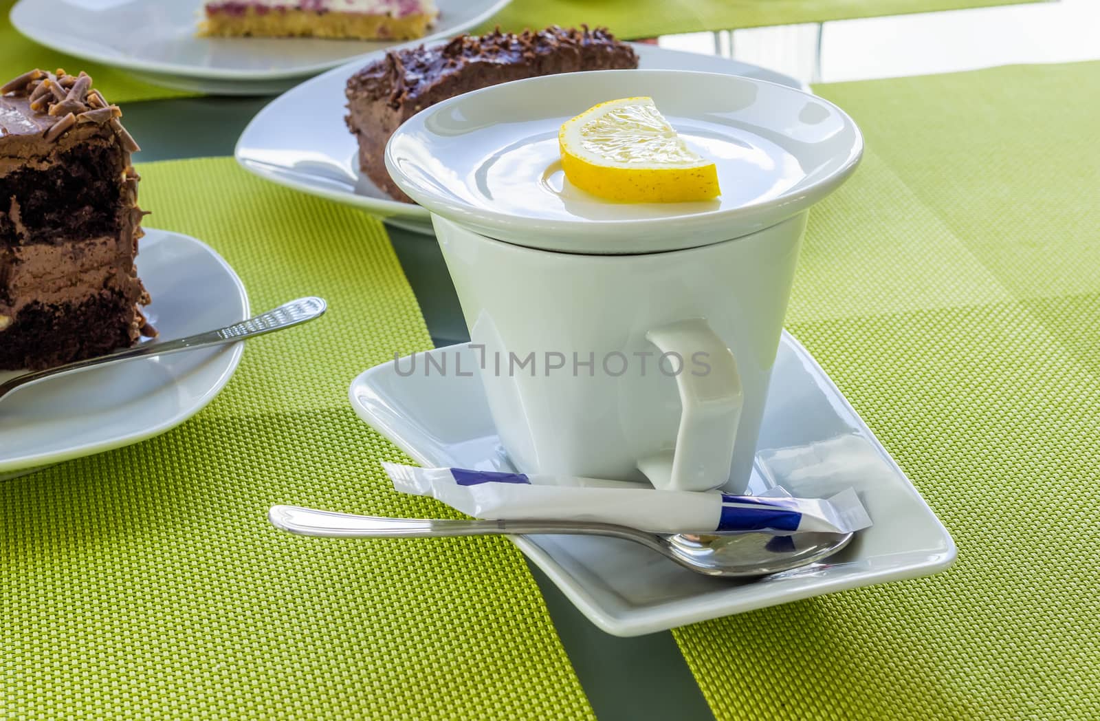White porcelain cup of tea with lemon, sugar, spoon on a table in the cafeteria.