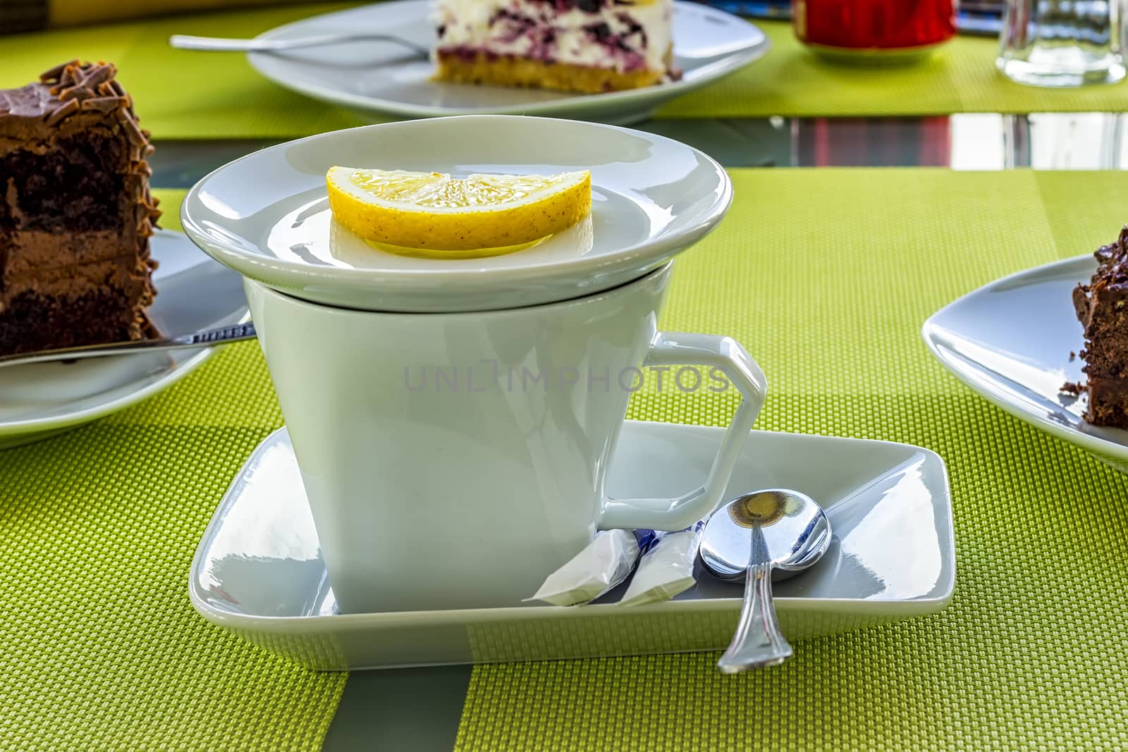 White porcelain cup of tea with lemon, sugar, spoon on a table in the cafeteria.