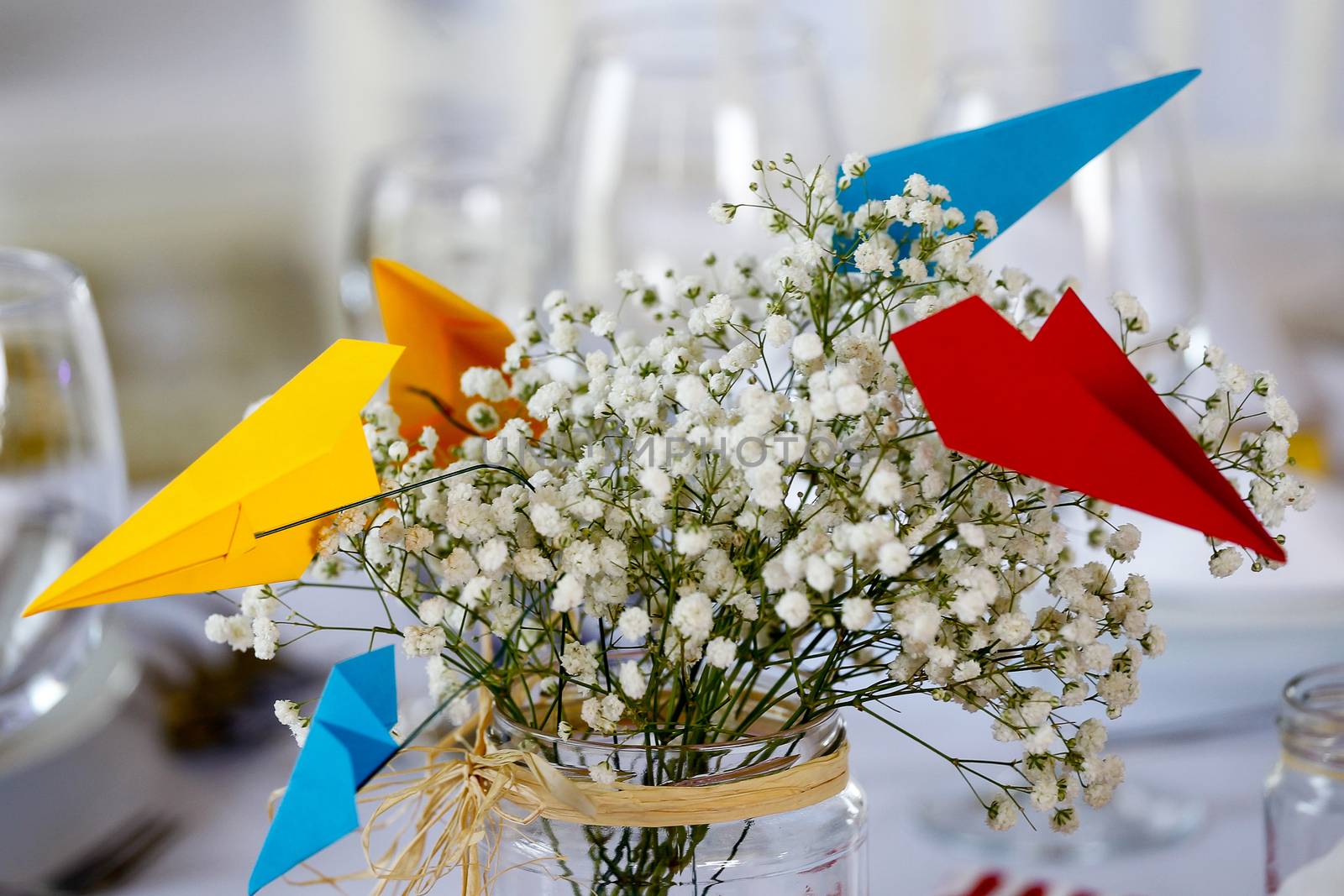 Circle dinner table served with white crockery and decorated with colorful objects.