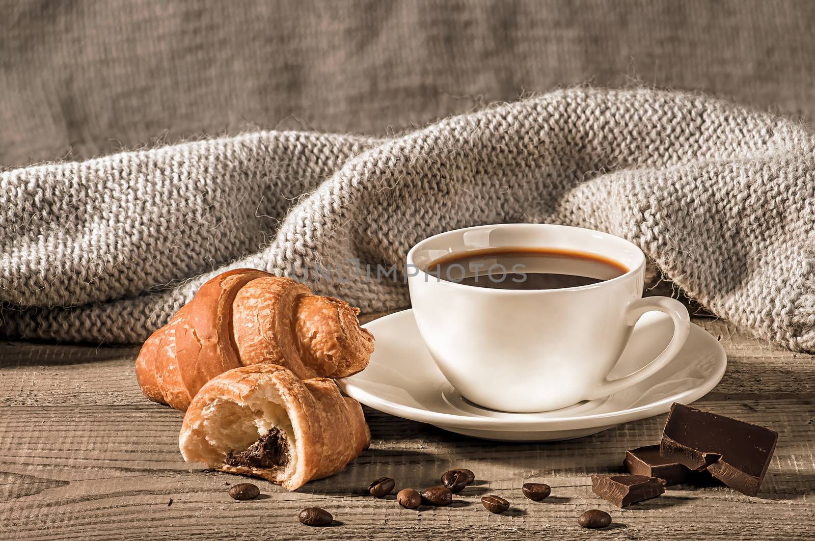 Coffee with croissants on the background of a woolen scarf. Grains of coffee next to the cup. Several pieces of dark chocolate next to each other.