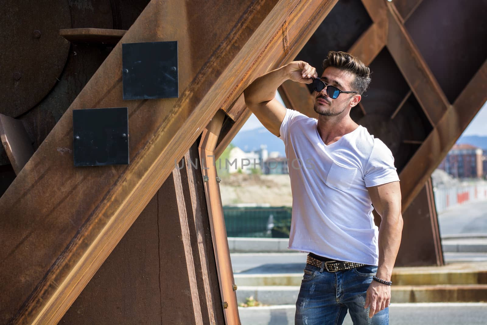 Handsome man in sunglasses and white T-shirt leaning on supports.