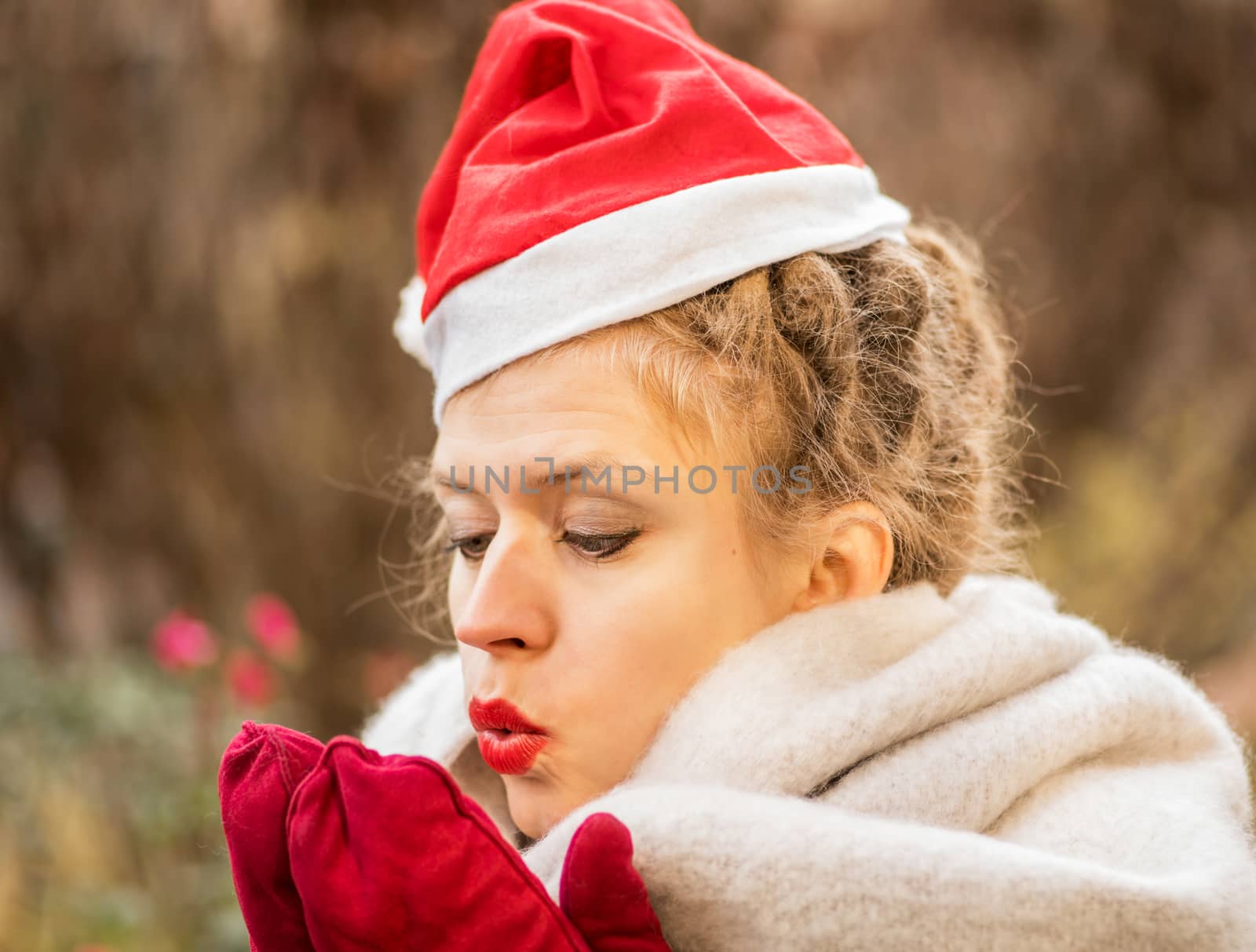christmas concept. european woman wearing warm scarf and christmas hat is blowing on her hands