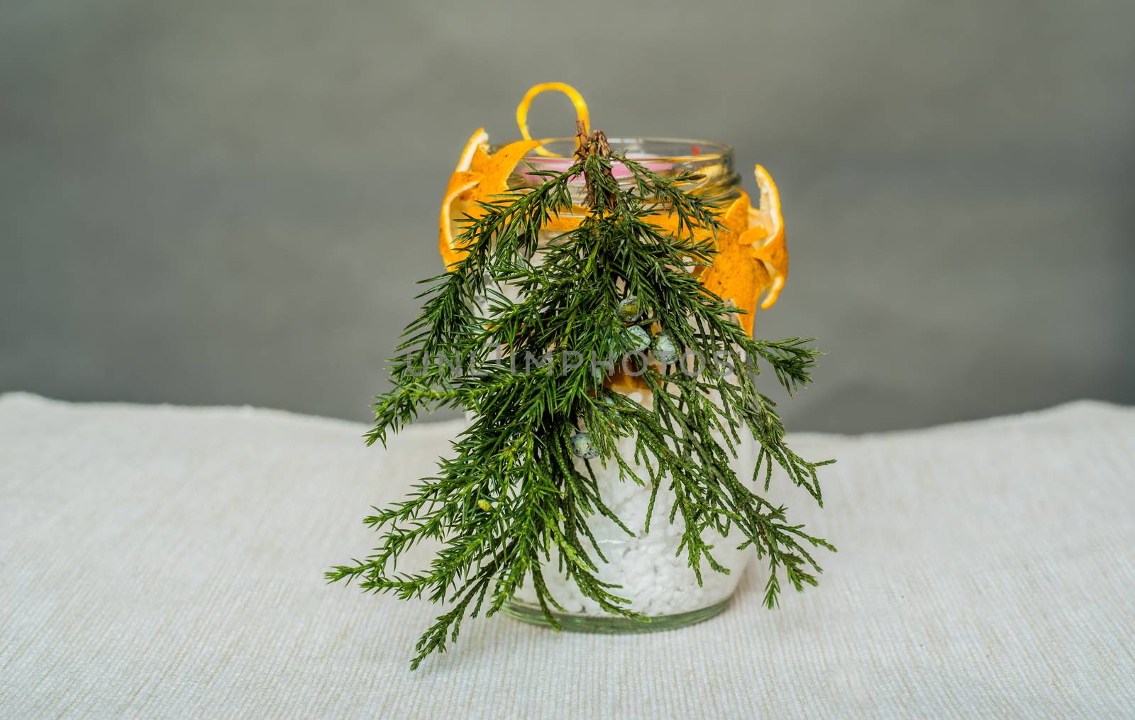 Christmas decorations on the table, hand made candle in a glass bottle with orange peel stars and fir tree branch