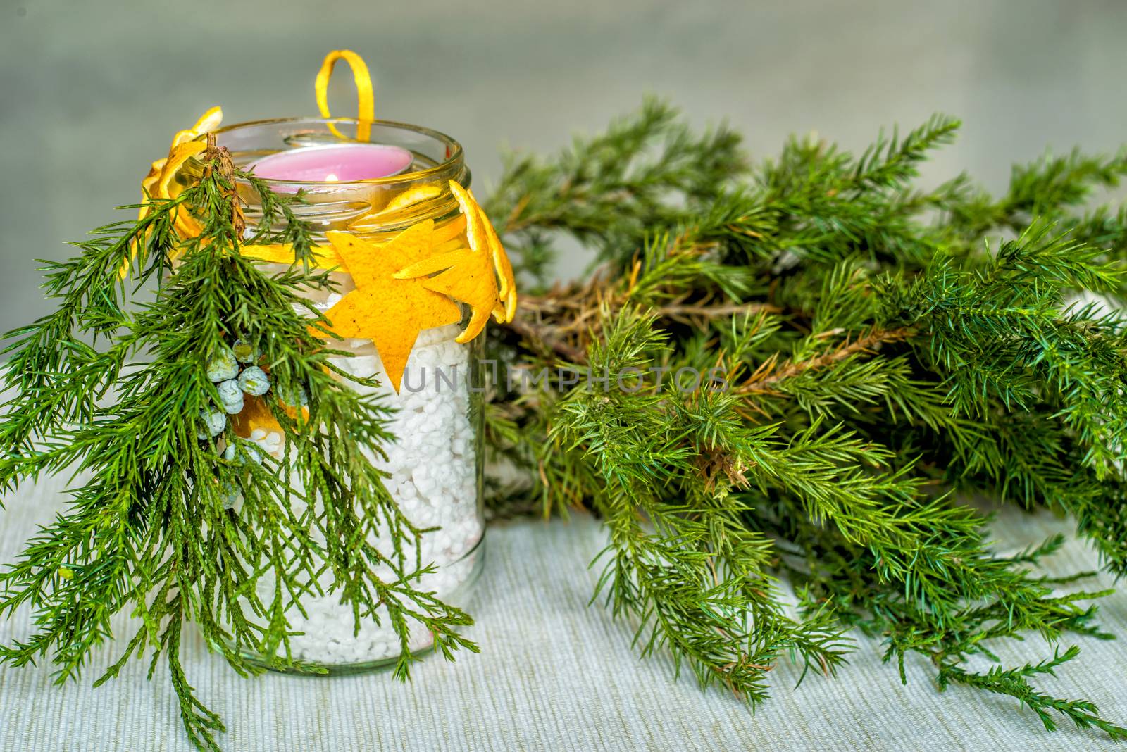 Christmas decorations on the table, hand made candle in a glass bottle with orange peel stars and fir tree branch ,tablecloth and fir tree branch
