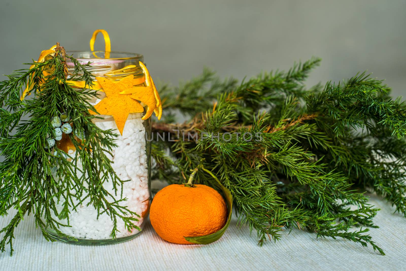 Christmas decorations on the table, hand made candle in a glass bottle with orange peel stars and fir tree branch ,tablecloth,tangerine and fir tree branch