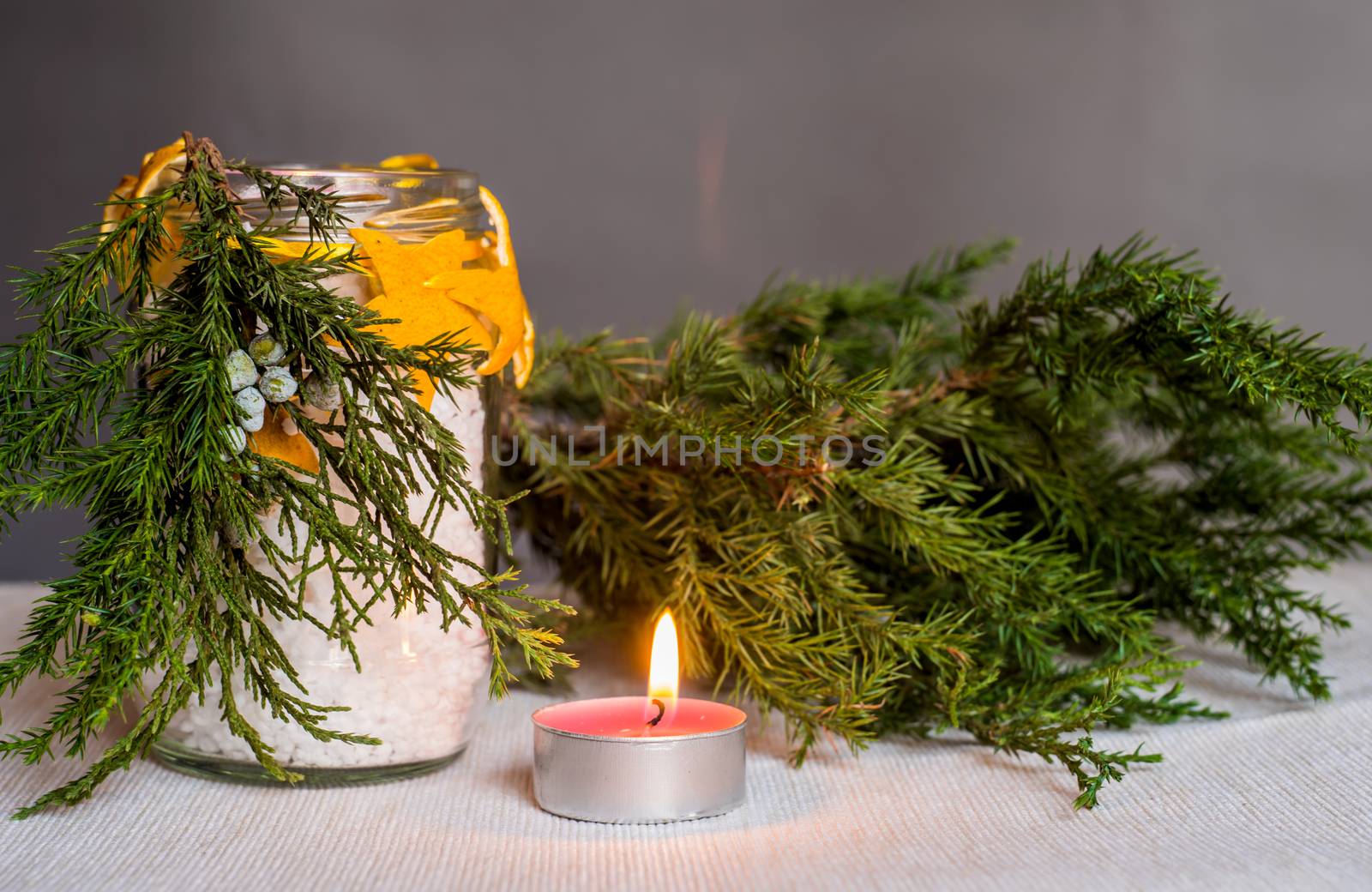 Christmas decorations on the table, hand made candle in a glass bottle with orange peel stars and fir tree branch ,tablecloth,tangerine and fir tree branch