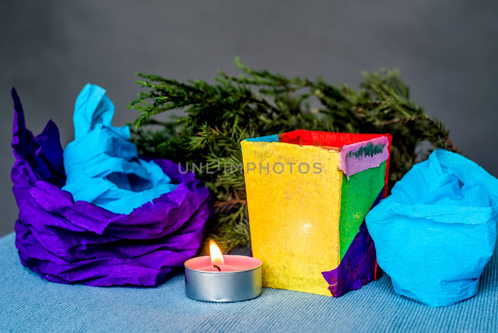 christmas craft composition on the blue tablecloth. candle with fir tree branch, crepe paper and blue tablecloth