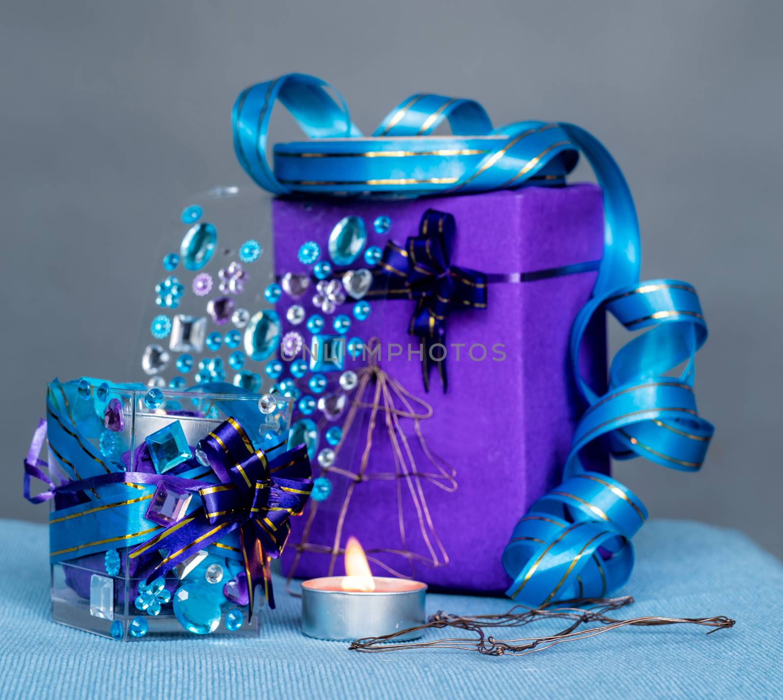 christmas craft composition on the blue tablecloth. candle with gems and blue ribbon, a gift and xmas tree decorations