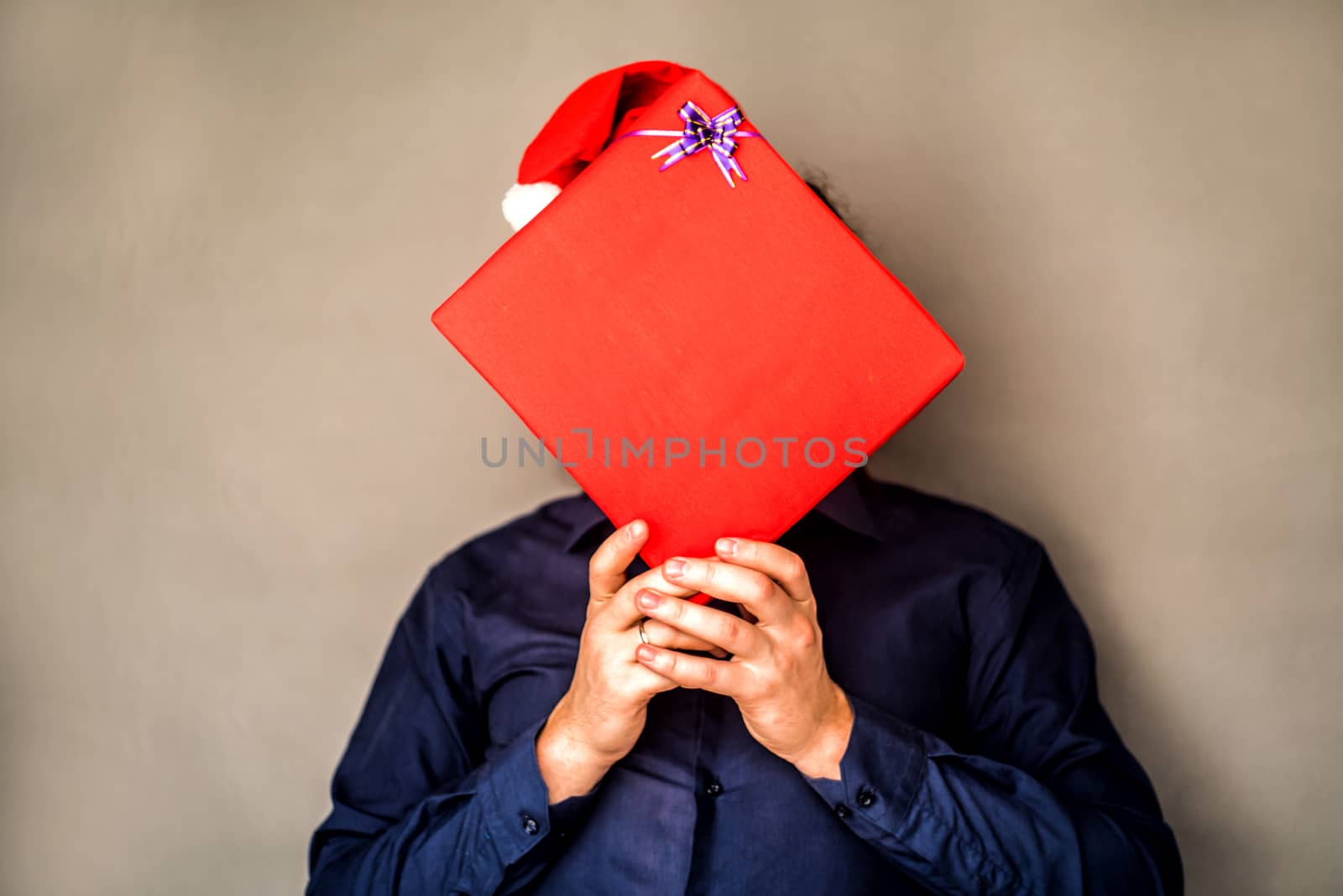 man in a christmas hat covers his face with a present by Desperada