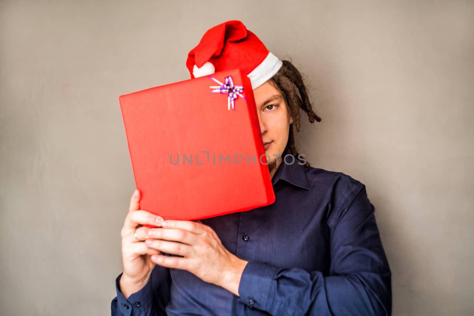 caucasian man with afro hairstyle and santa hat covering his face with a christmas present by Desperada