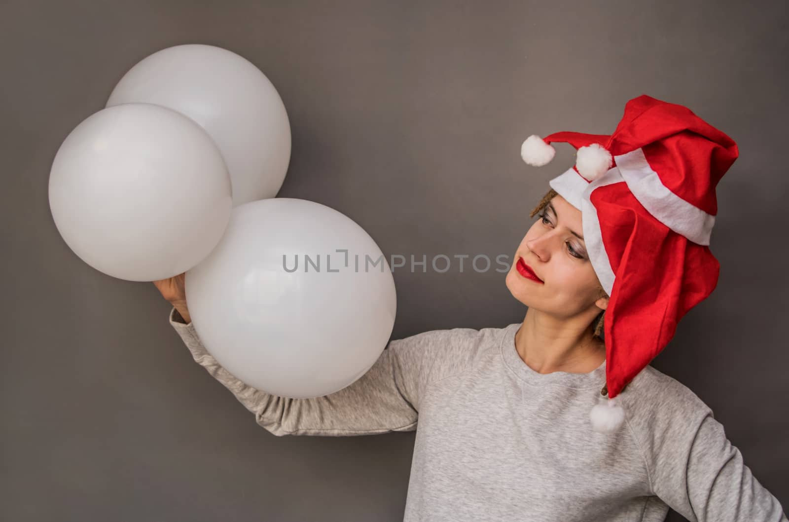 smiling womanwith red lips in santa hats with tree white balloons on grey background