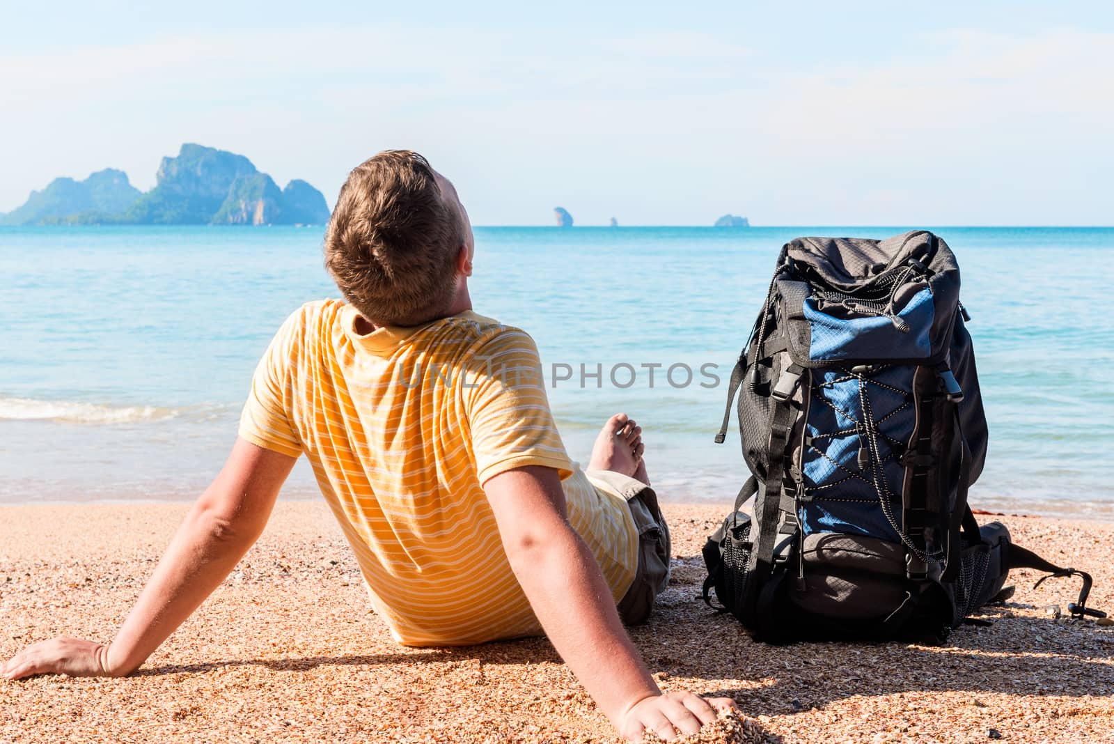 tourist with a large backpack relaxes on the beach near the sea with a beautiful view of the mountains