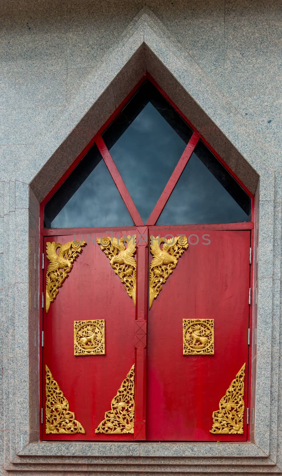 red window shutters decorated with gold ornaments on a temple in Thailand closeup