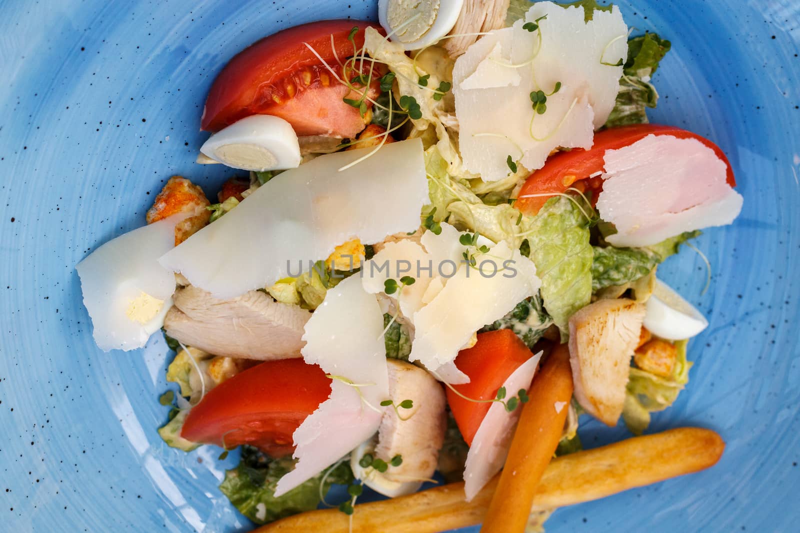 Fresh salad of chicken with vegetables and cheese, on a blue background