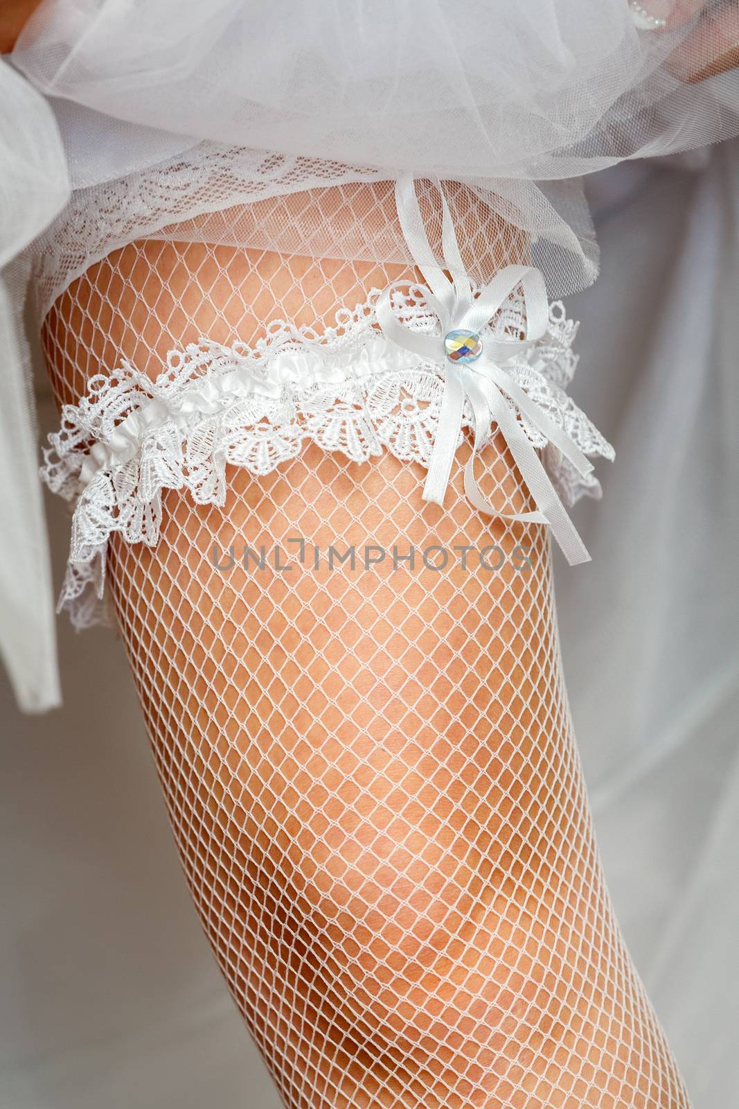 A white lace Garter on the leg of a bride by fogen