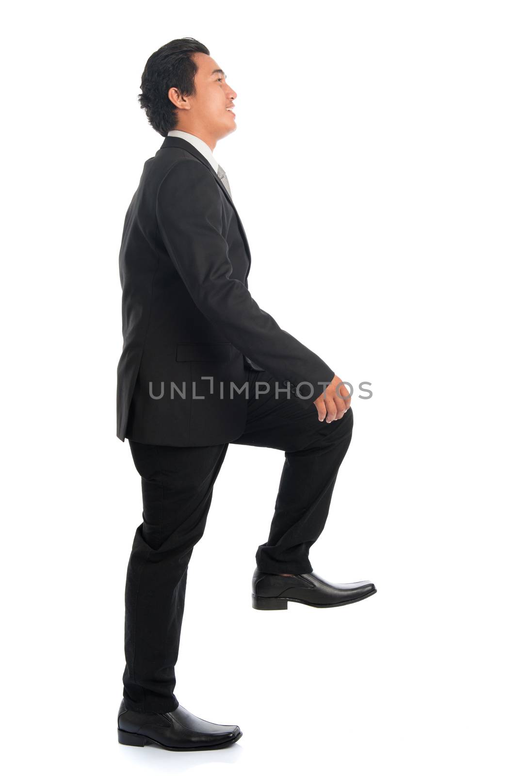 Full body side view of attractive young Southeast Asian businessman stepping up stair case, isolated on white background. 