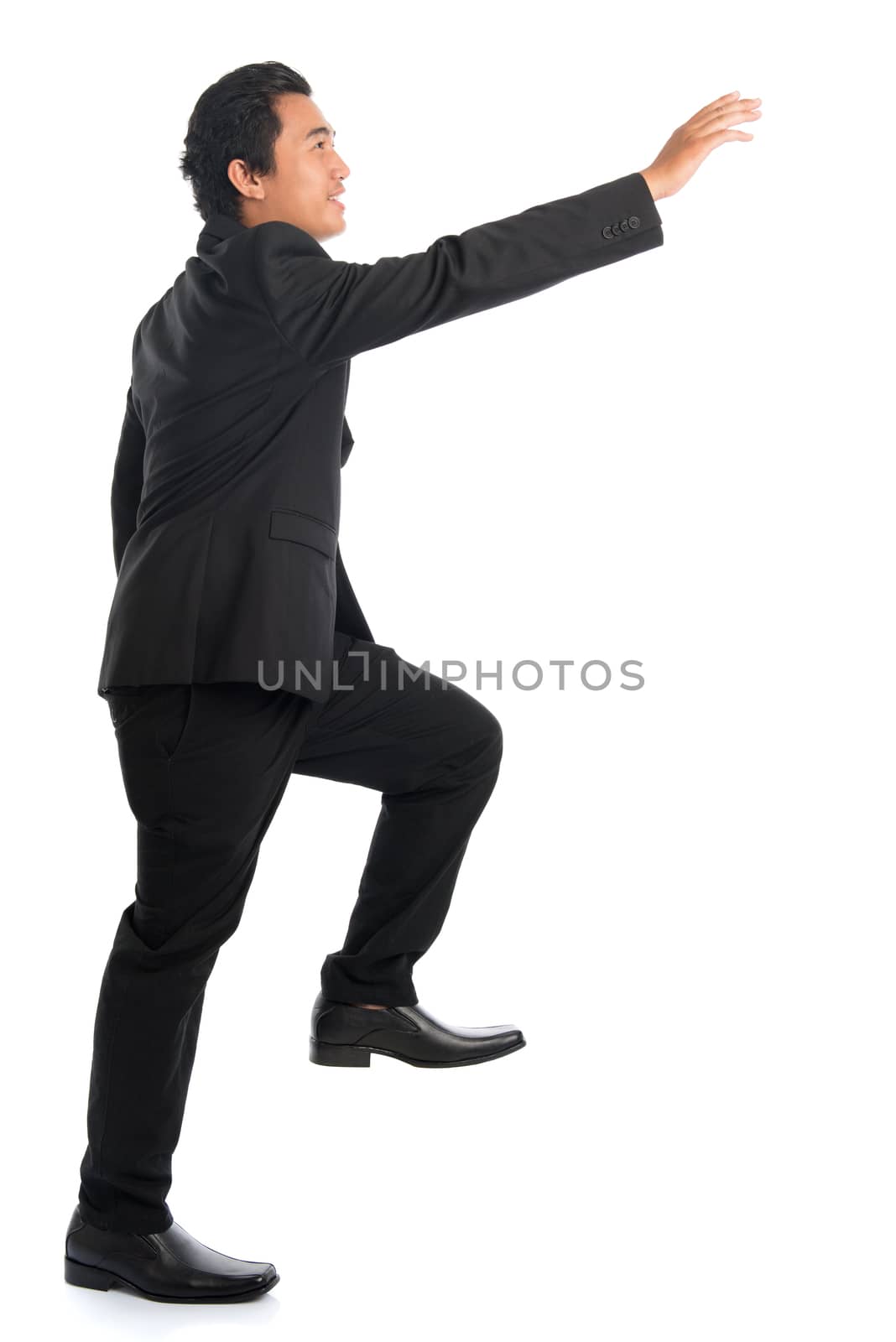 Full body side view of attractive young Southeast Asian businessman stepping up stair case and hand reaching something, isolated on white background. 