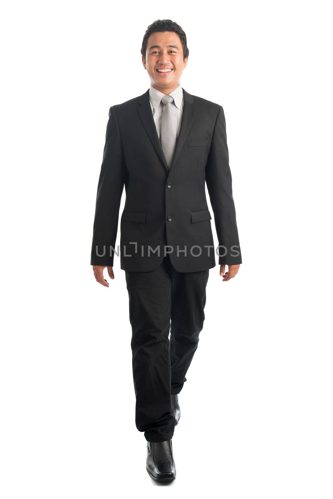 Full body front view portrait of smart young Southeast Asian businessman walking, isolated on white background. 