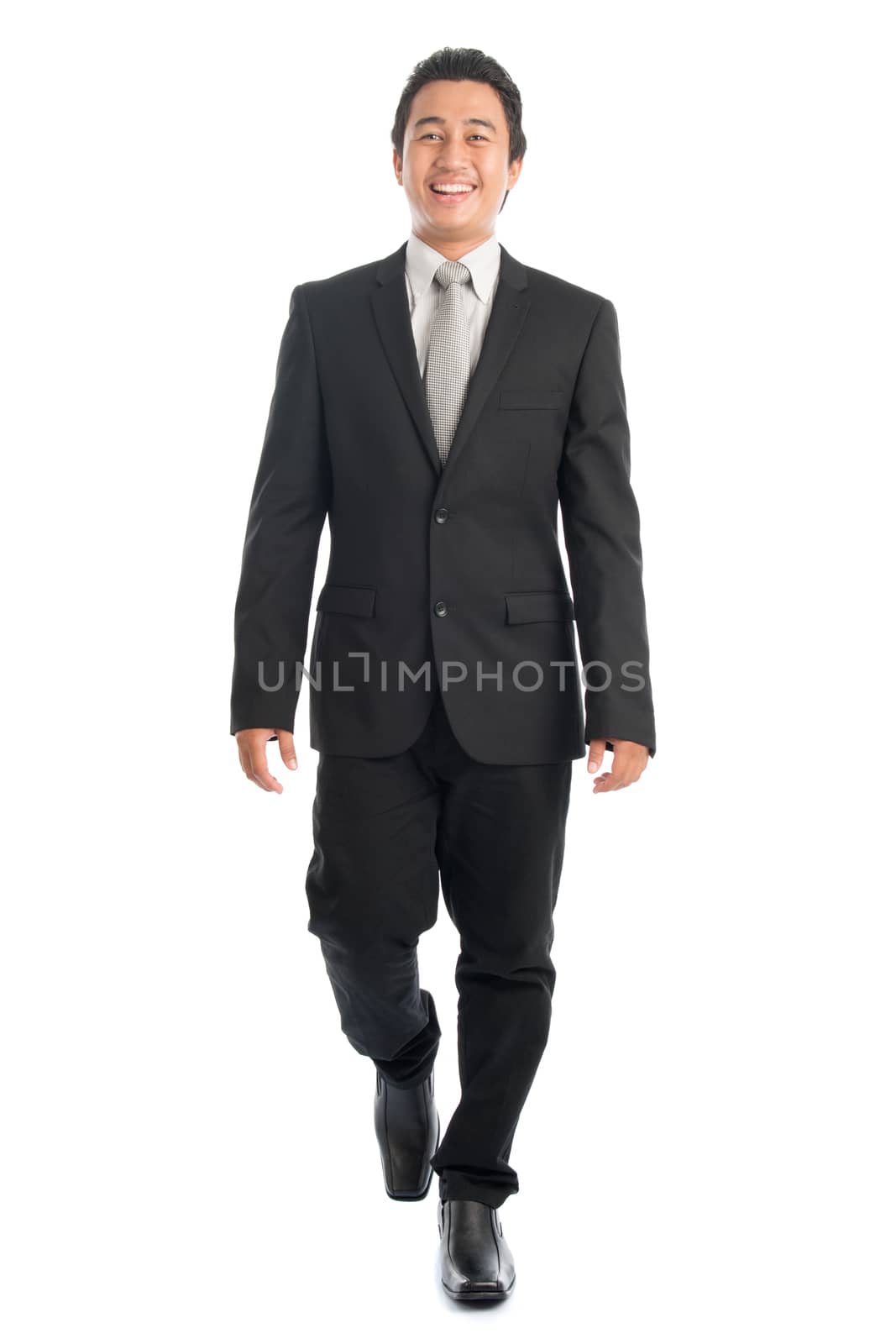 Full body front view portrait of happy young Southeast Asian businessman walking, isolated on white background. 