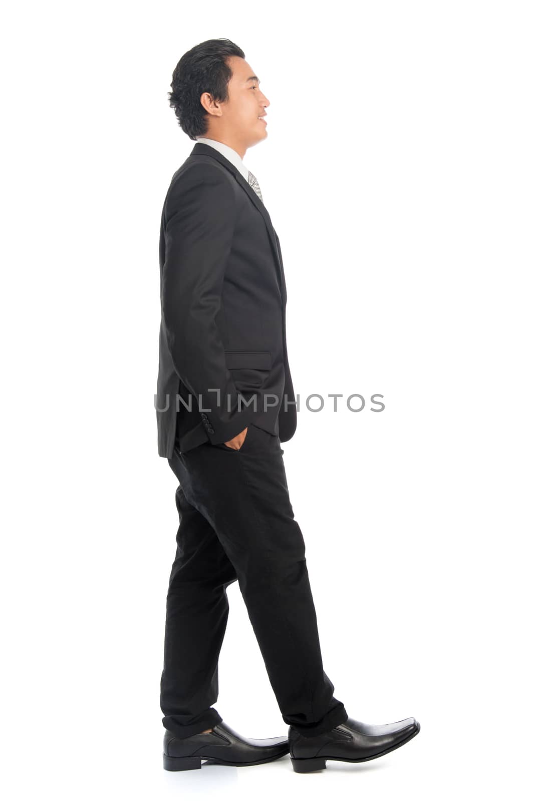 Full body side view of attractive young Southeast Asian businessman walking, isolated on white background. 