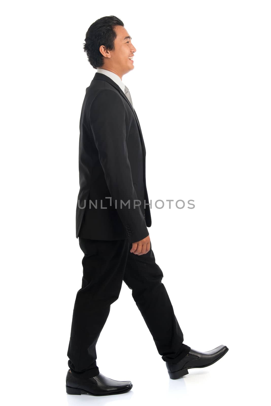 Full length side view of handsome young Southeast Asian businessman walking, isolated on white background. 