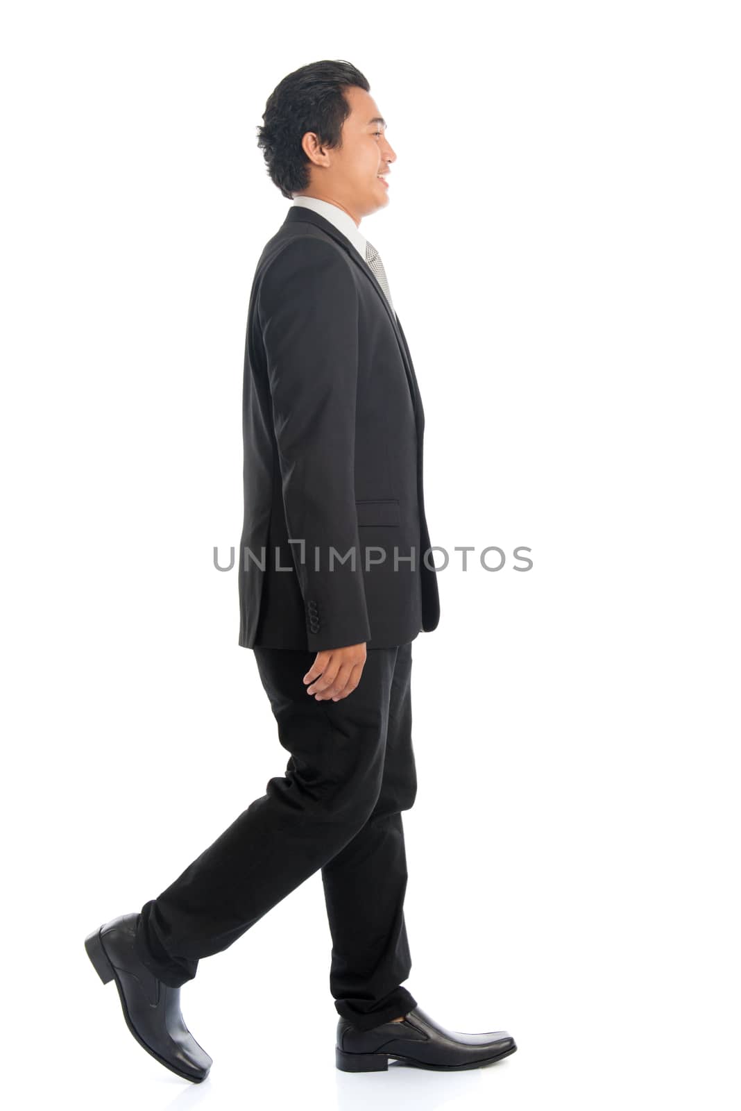 Full length side view of attractive young Southeast Asian businessman walking, isolated on white background. 