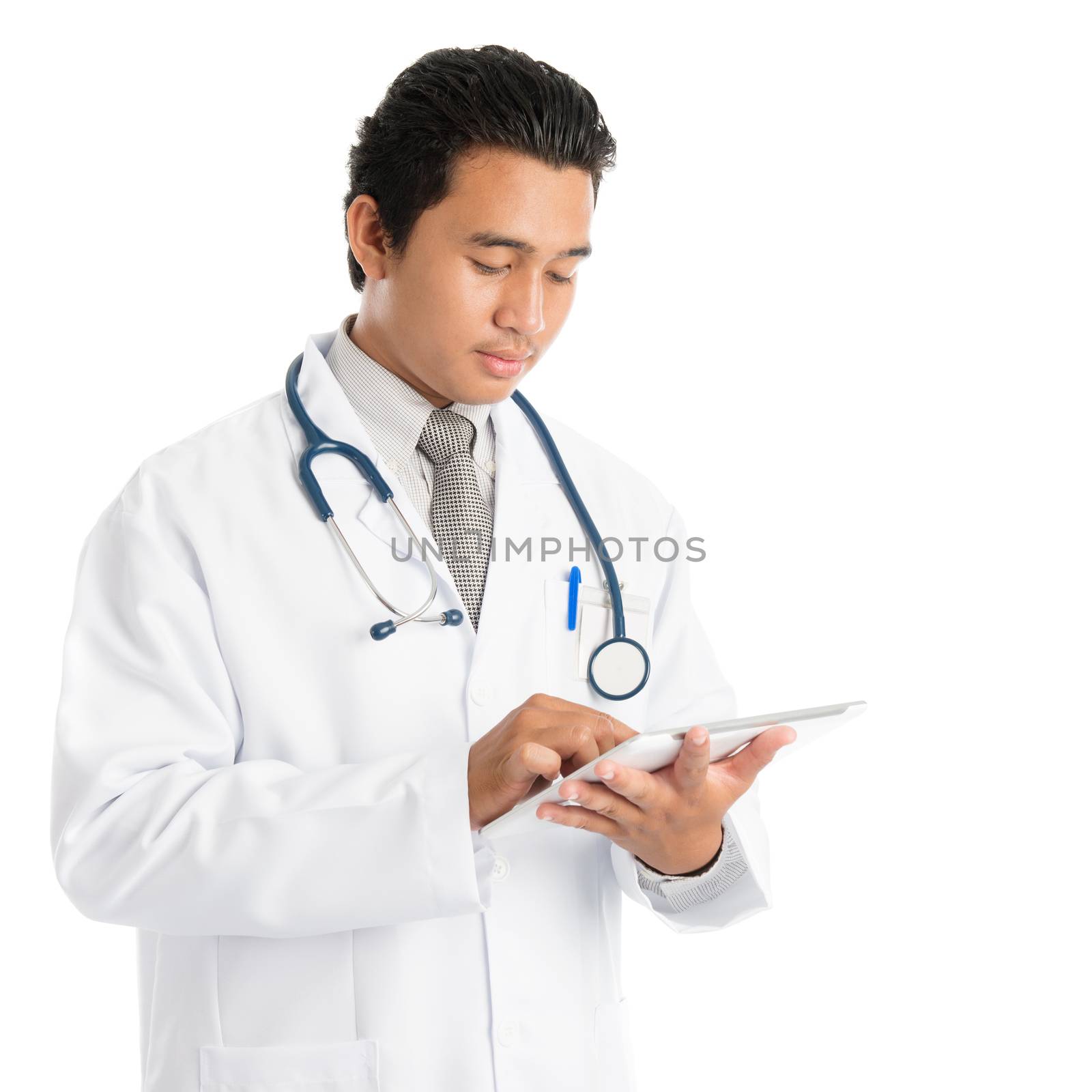 Portrait of attractive young male Southeast Asian medical doctor using tablet pc, standing isolated on white background.