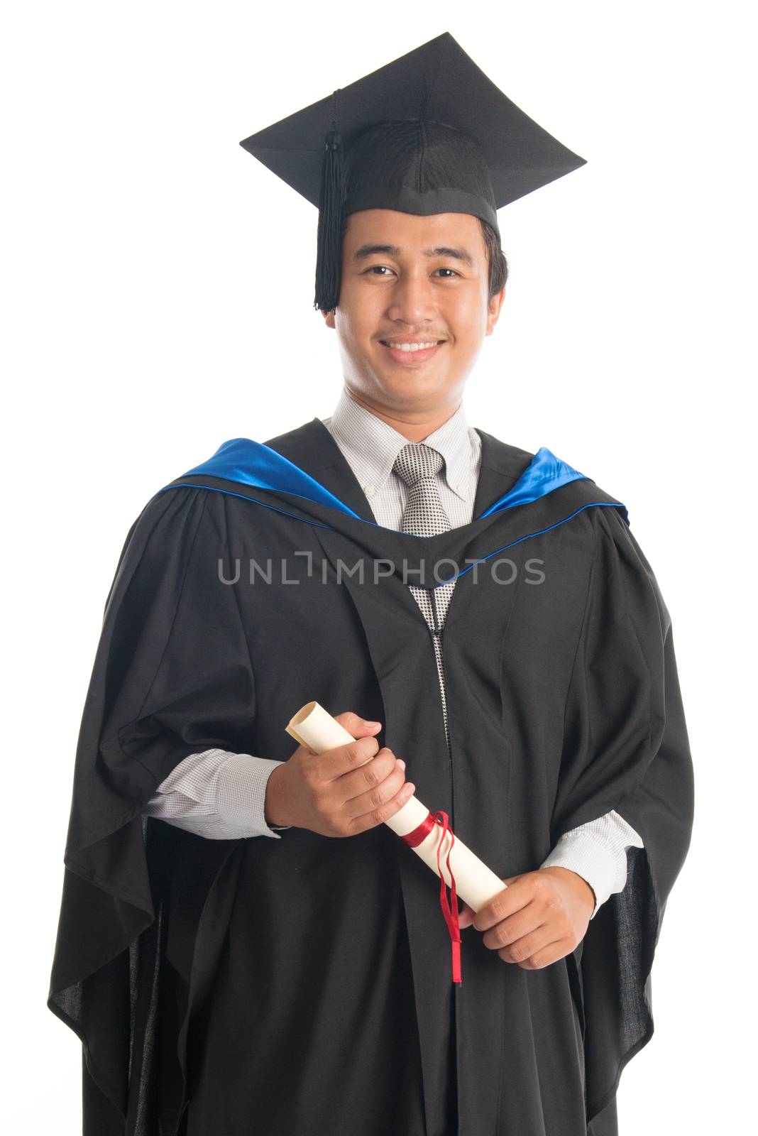 Happy male university student in graduation gown holding paper certificate, standing isolated on white background. Attractive Southeast Asian model.