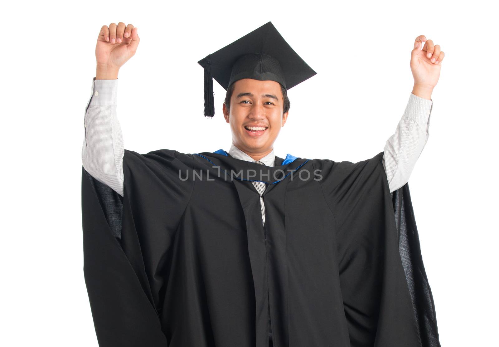 Attractive Southeast Asian male university student in graduation gown arms raised celebrating success, standing isolated on white background. 