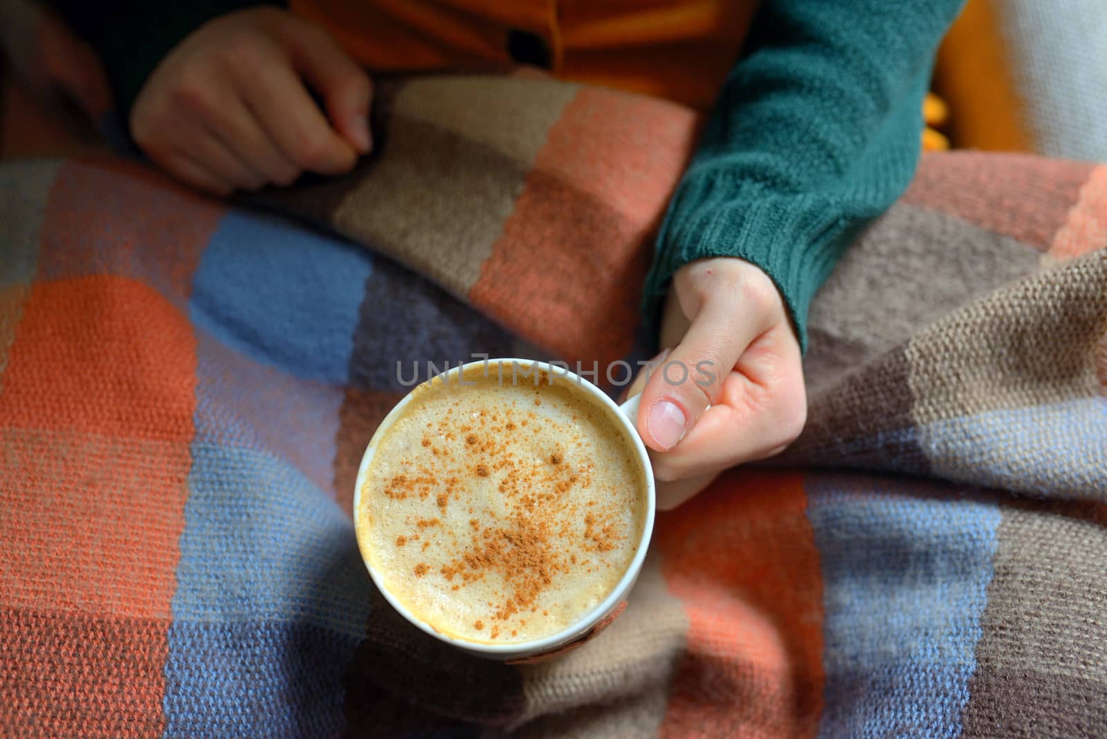Woman holding hot cup of cappuccino on blanket