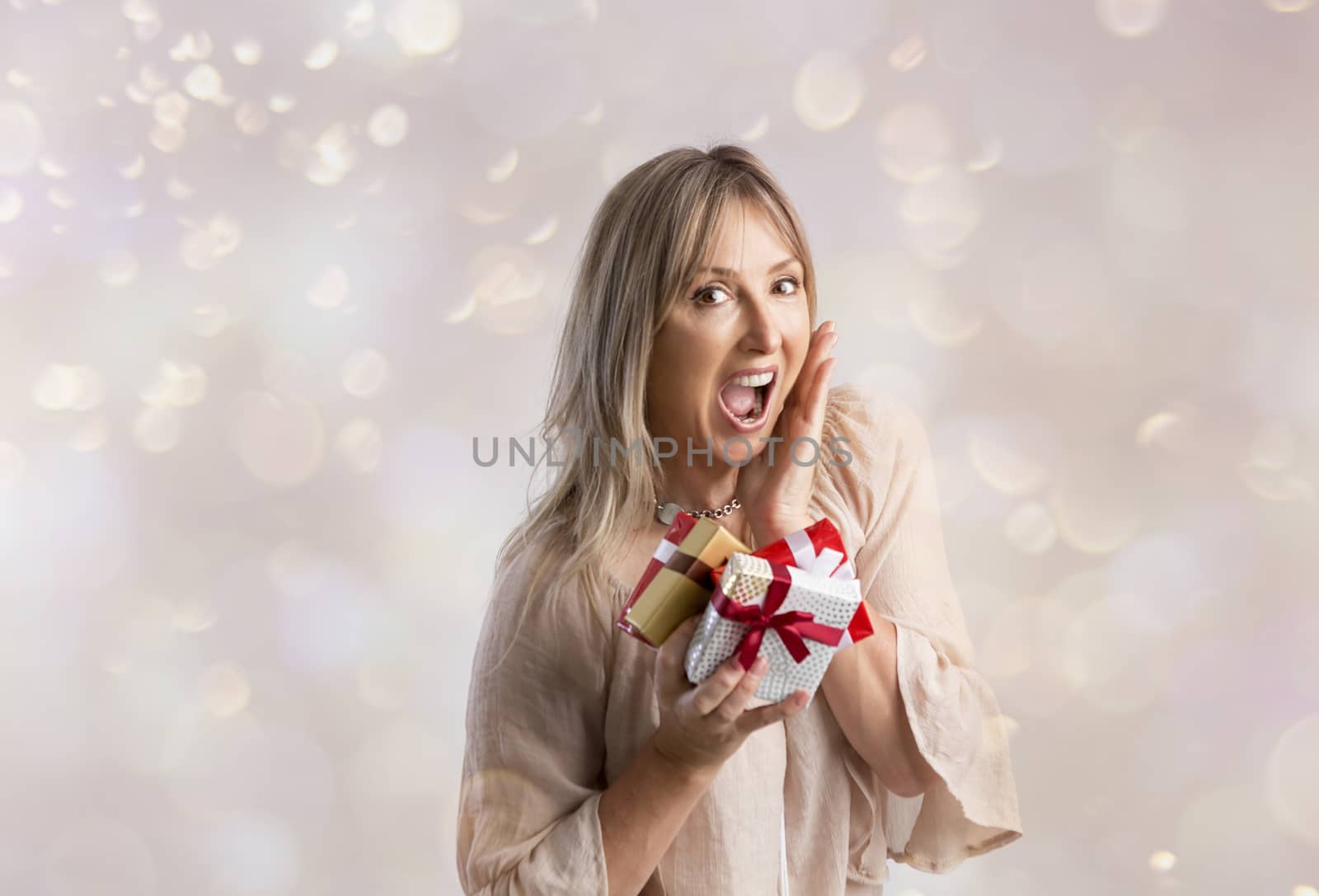 Surprised woman holding three wrapped Christmas presents tied up with ribbon.