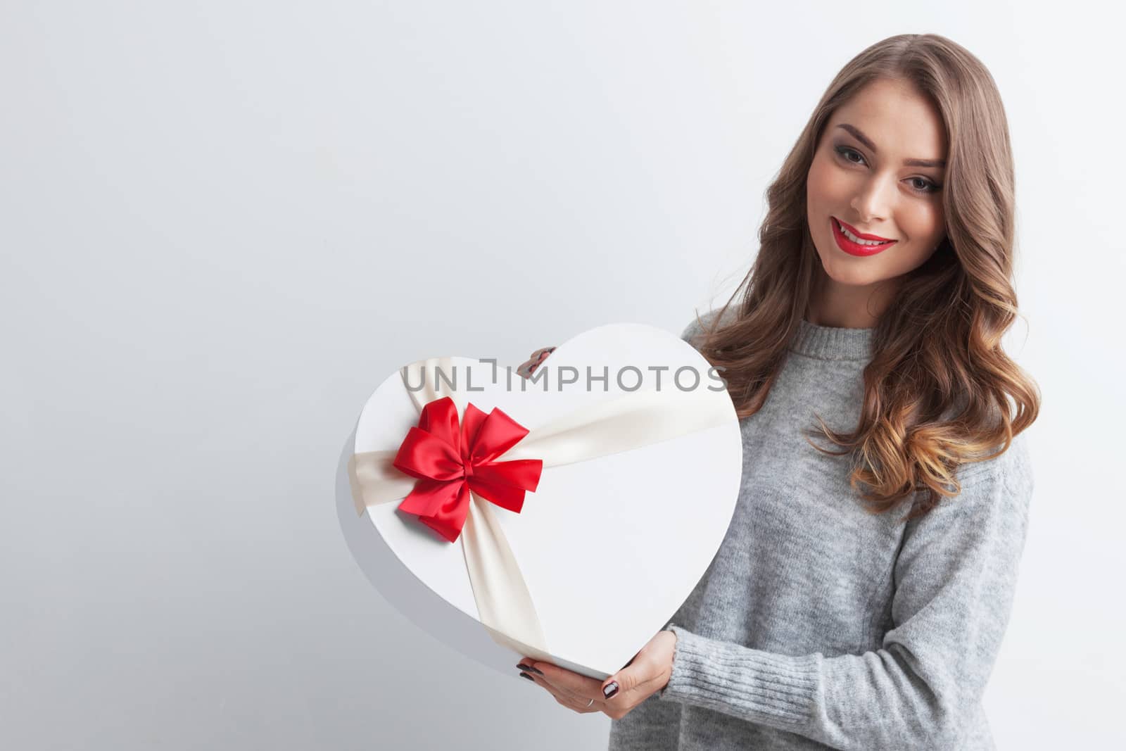 Young girl with red heart-shaped gift box on white background