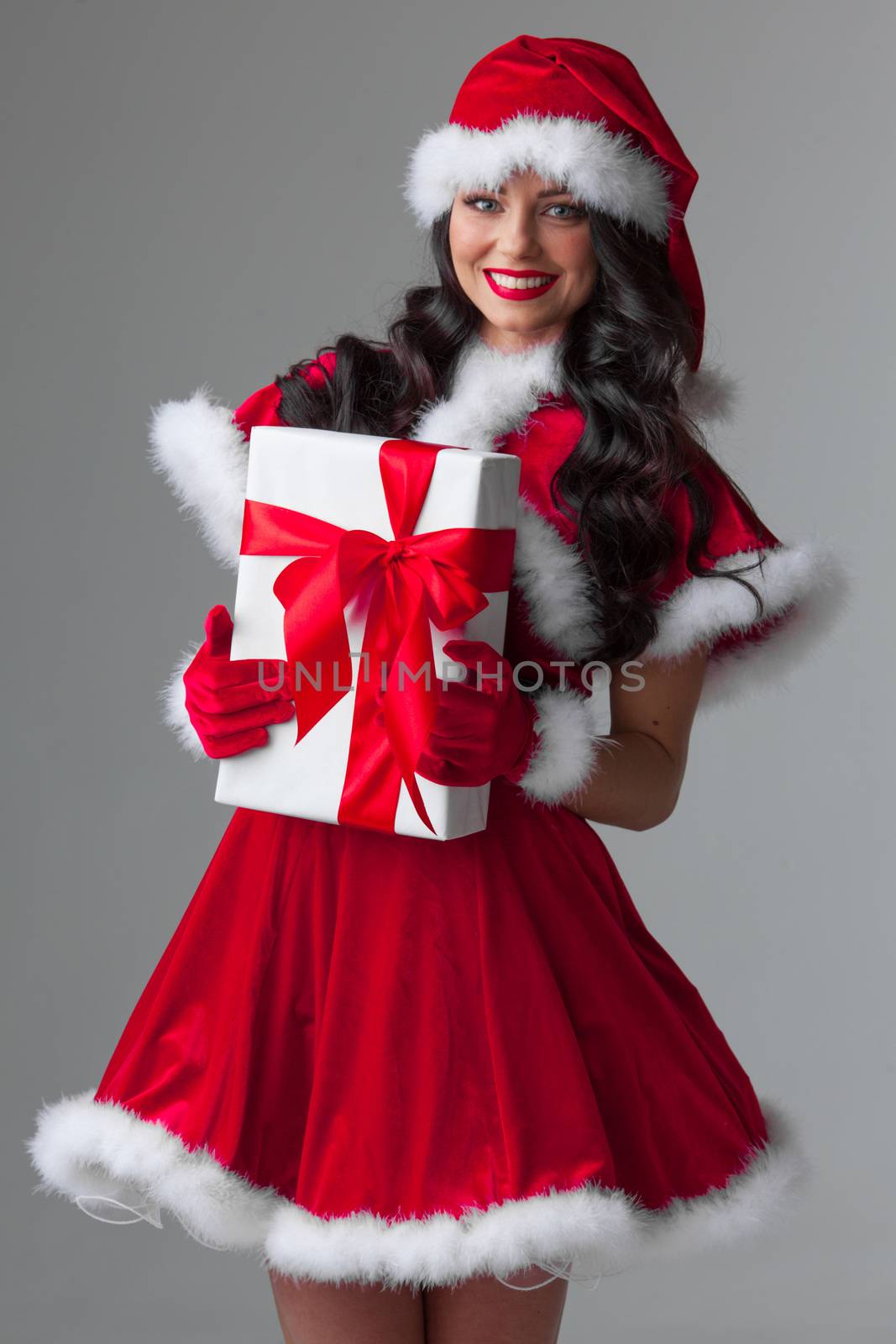 Beautiful young woman in Santa dress celebrating Christmas holding gift box