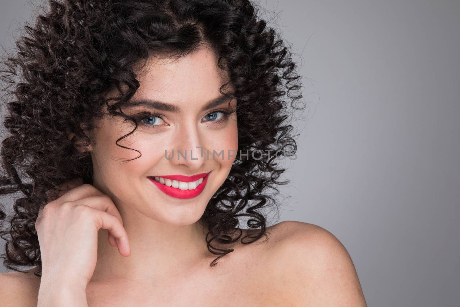 Portrait of beautiful smiling woman with curly hair, gray background