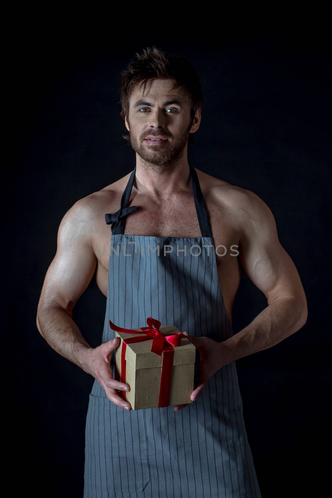 Handsome muscular naked man in an apron holding holiday gift box