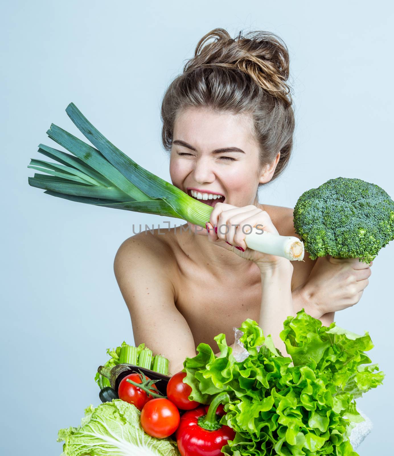 Happy smiling young woman with various vegetables biting leek