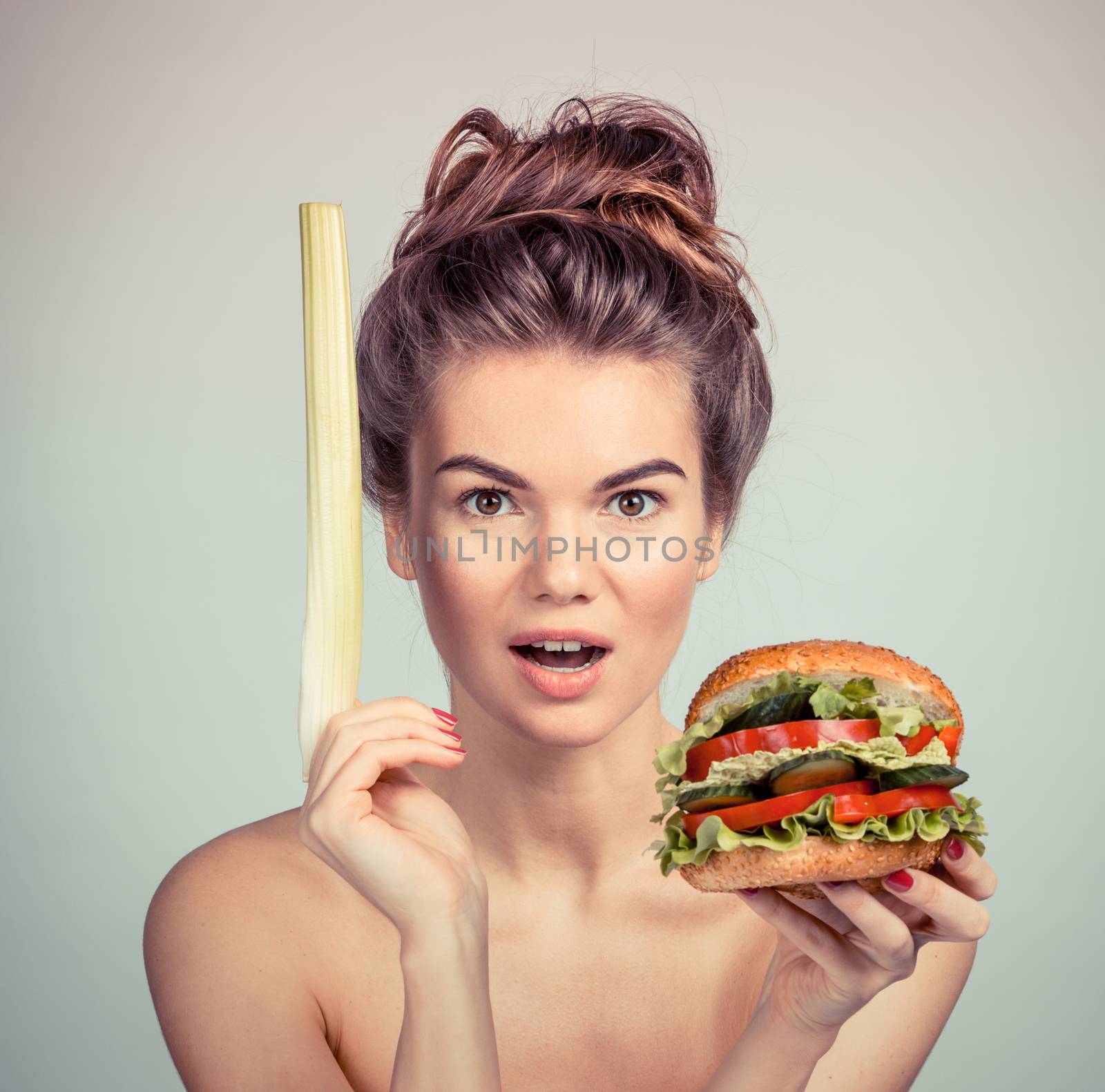 Young woman holding hamburger made of vegetables and stalk of celery, healthy eating concept