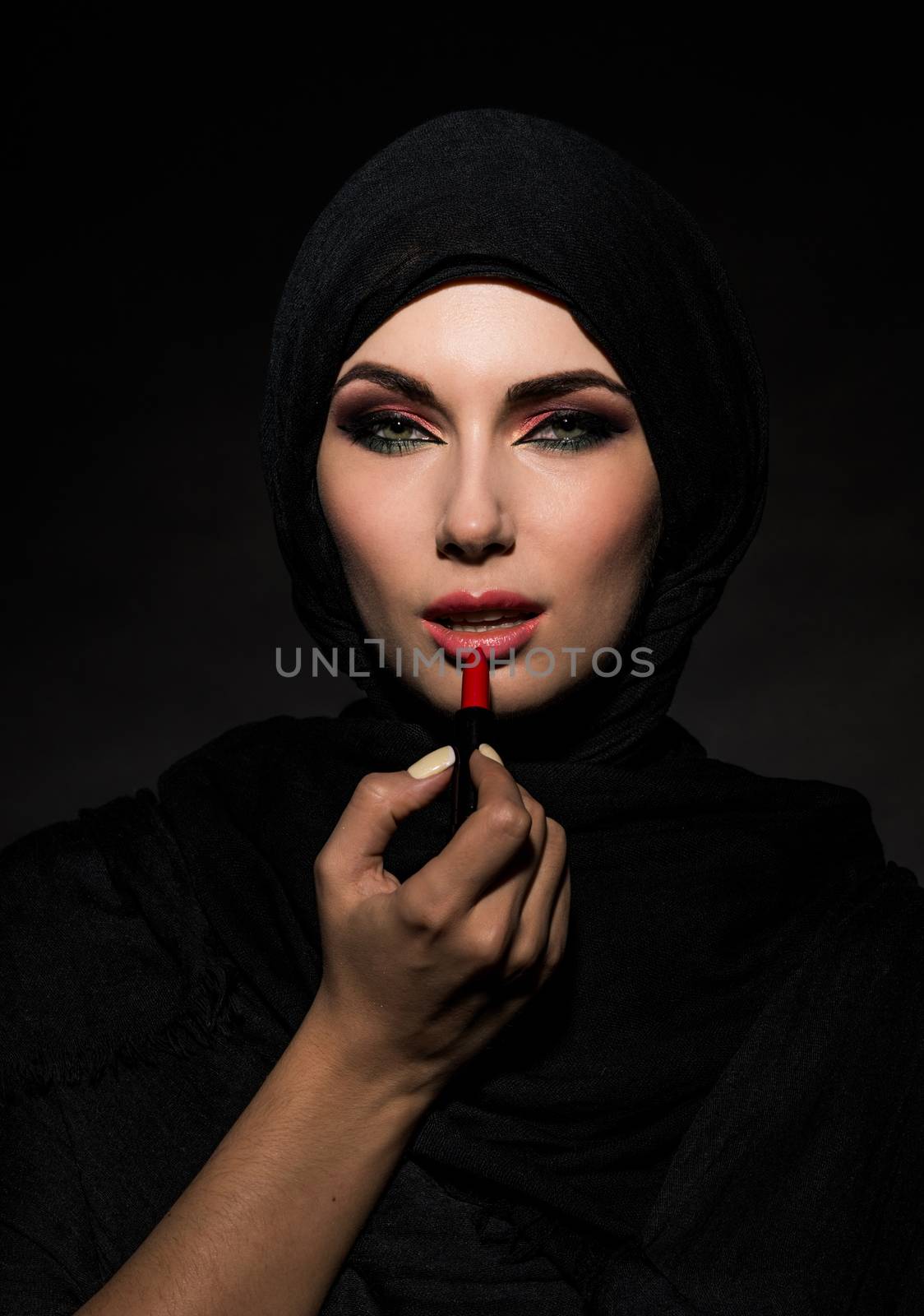 Young beautiful muslim woman putting red lipstick