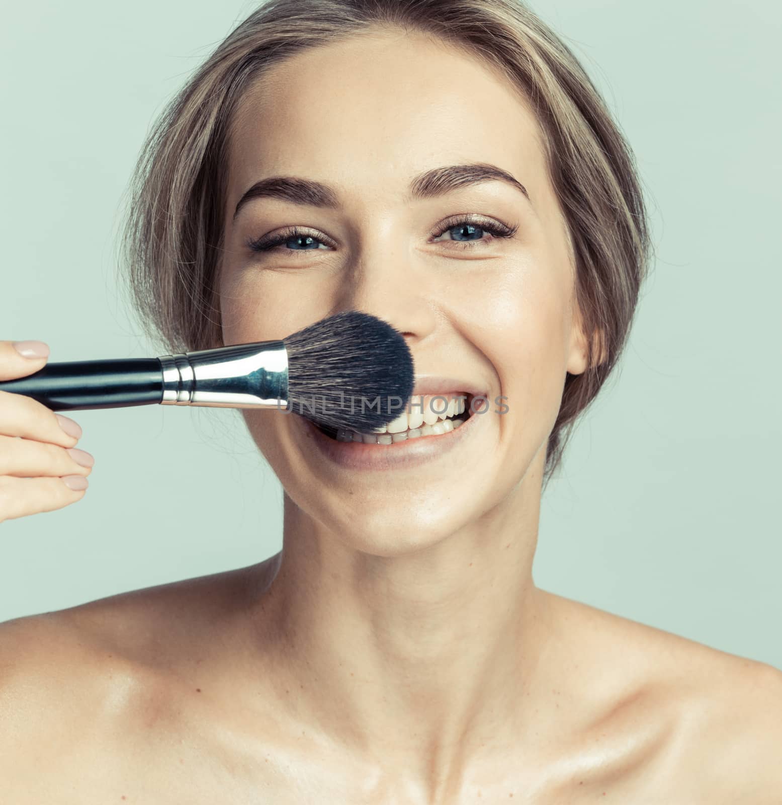 Portrait of a beautiful smiling woman applying make-up with a brush and making a funny face