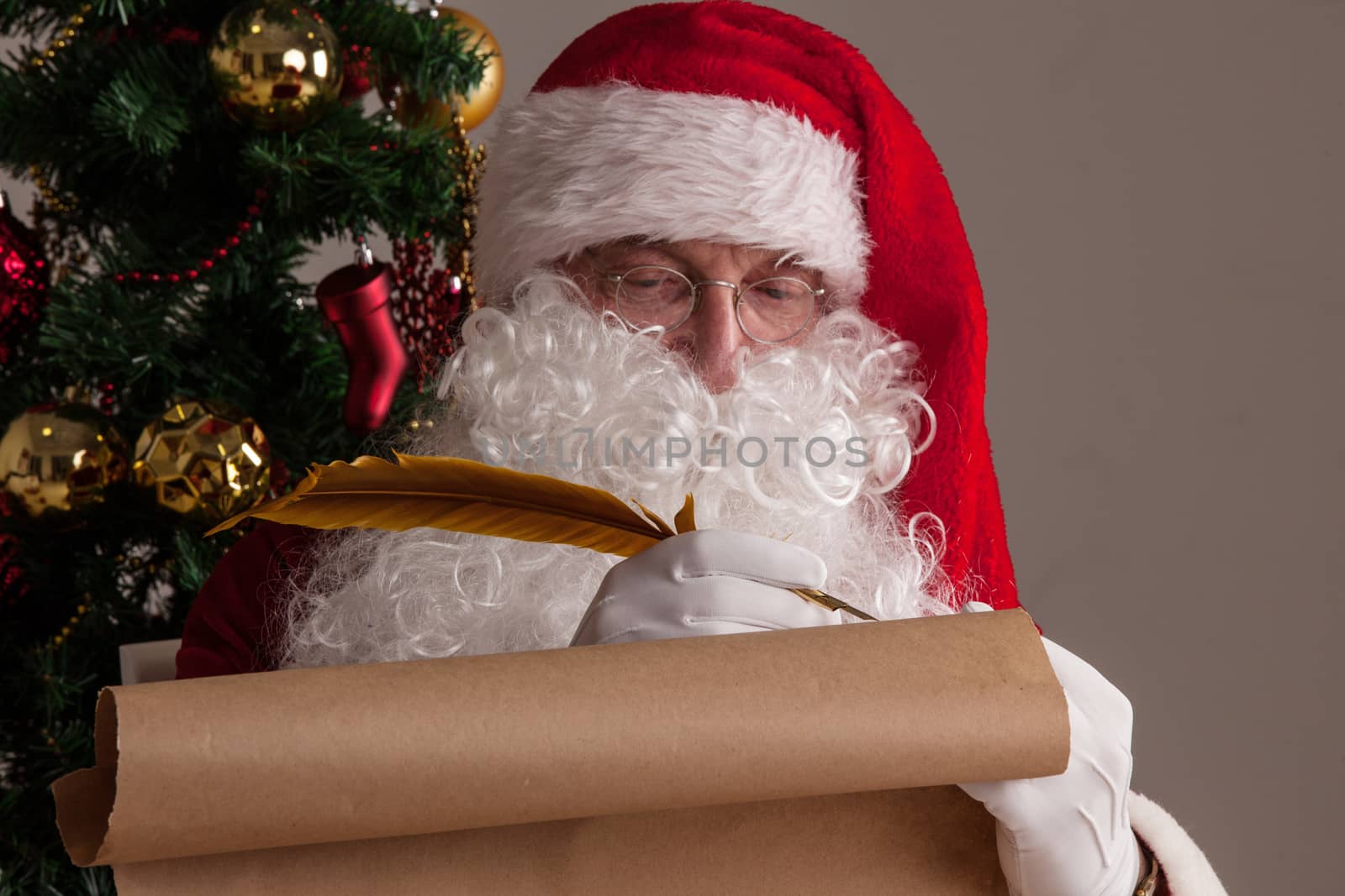 Santa Claus sitting at home and writing on old paper roll to do list with quill pen and ink