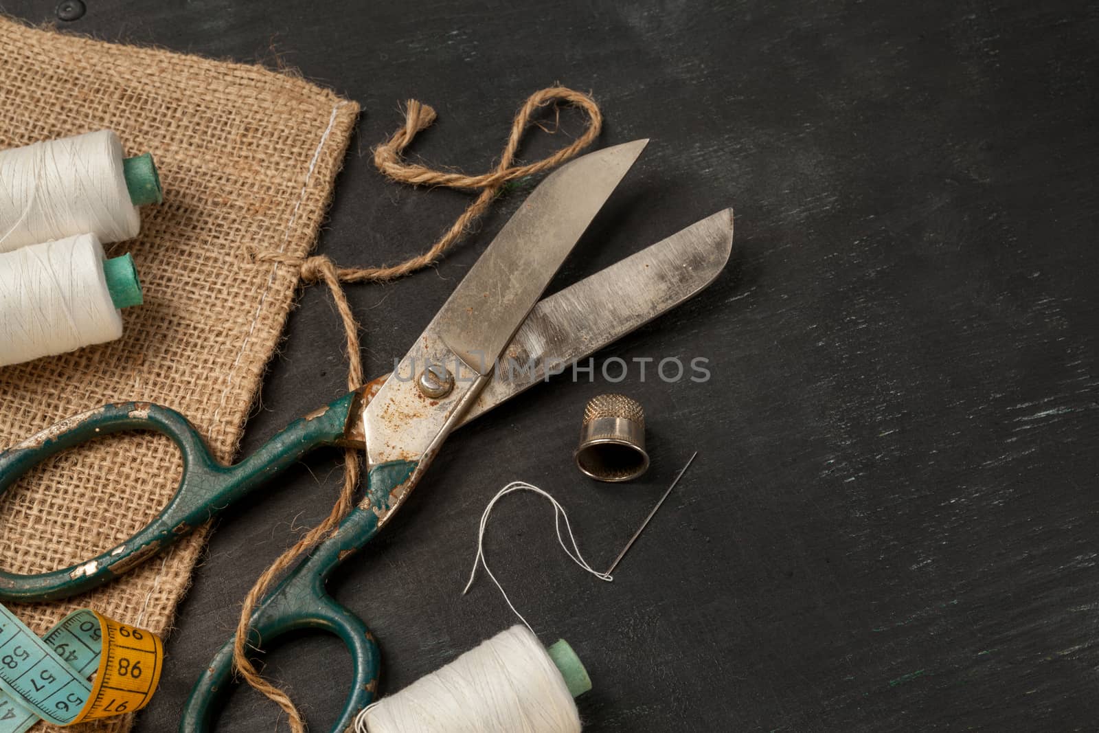 Retro sewing accessories - scissors, tape measure, thread on black wooden background. Horizontal closeup composition.