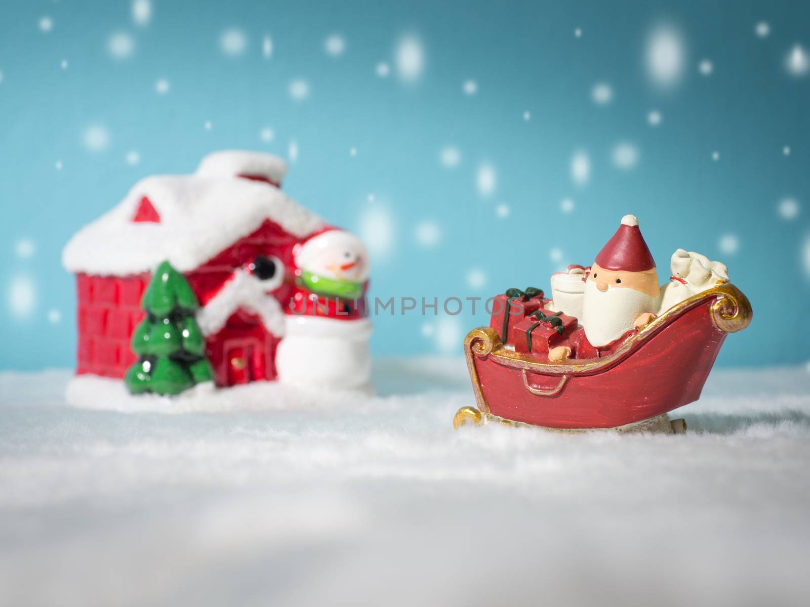 Happy Santa Claus with gifts box on the snow sled going to snow house. near snow house have Snowman and Christmas Tree. Santa Claus and snow house on the snow the background is powder blue. by PattyPhoto