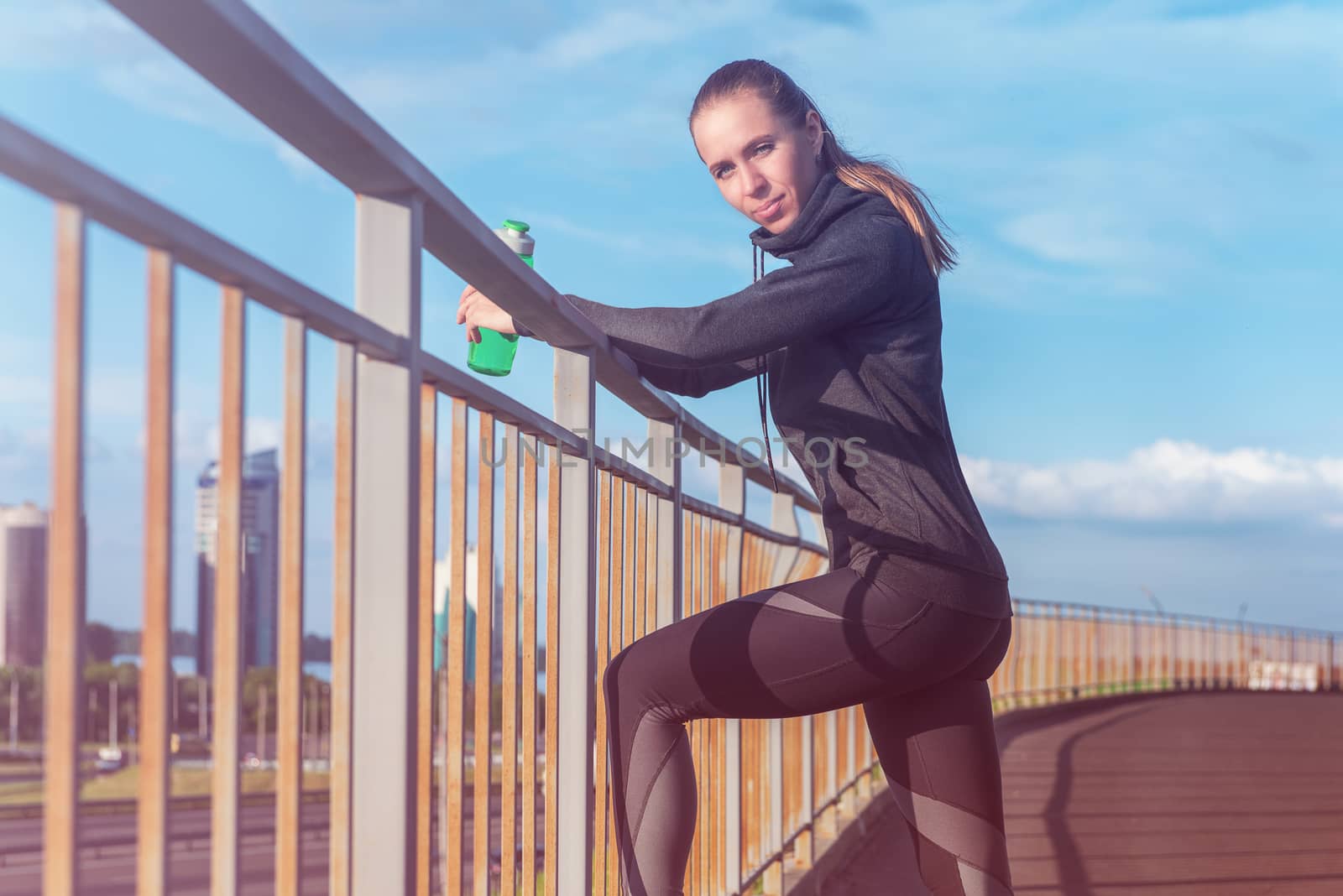 A woman in sportswear with bottle of water have rest at sunset on the evening city background