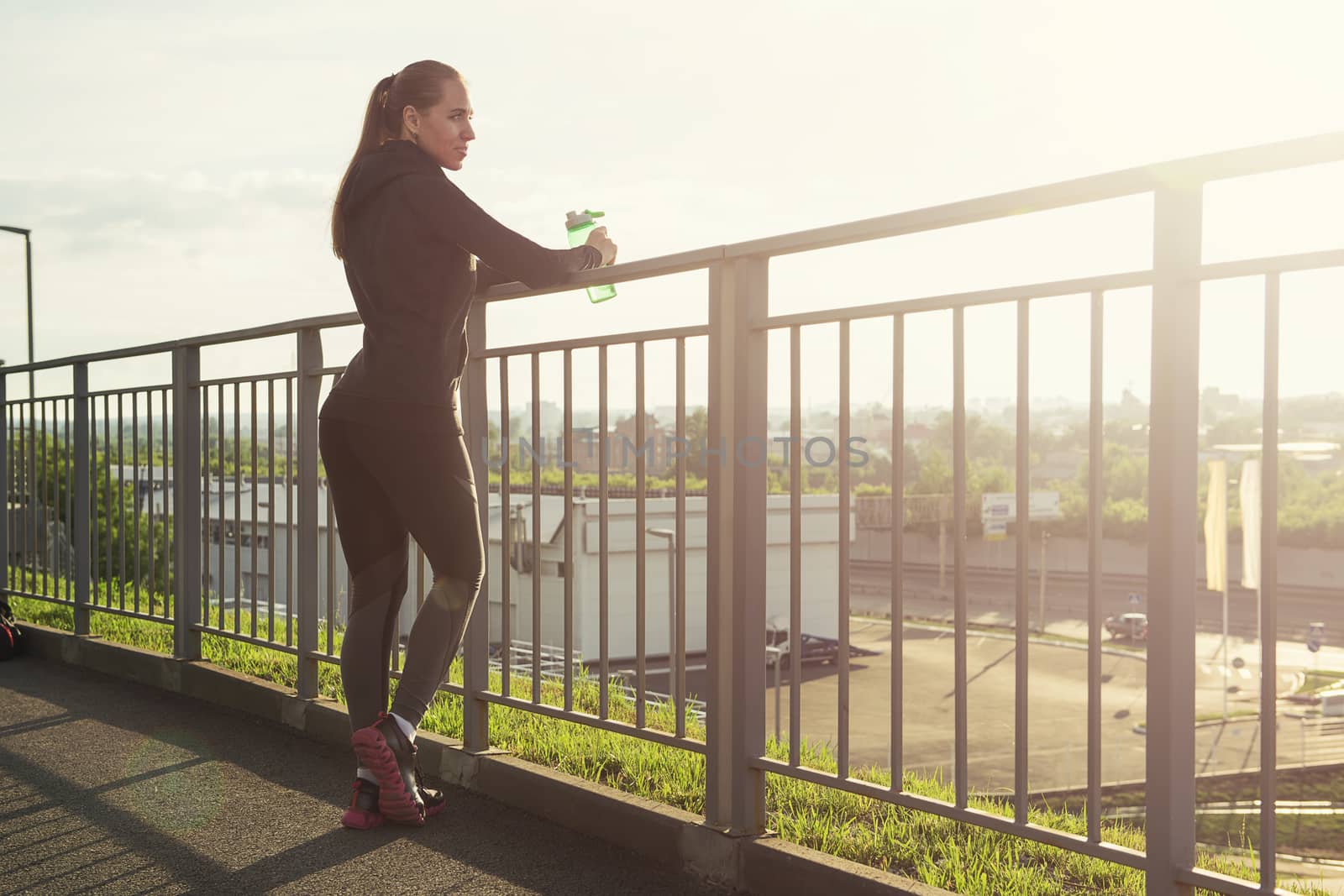 A woman in sportswear with bottle of water have rest at sunset on the evening city background