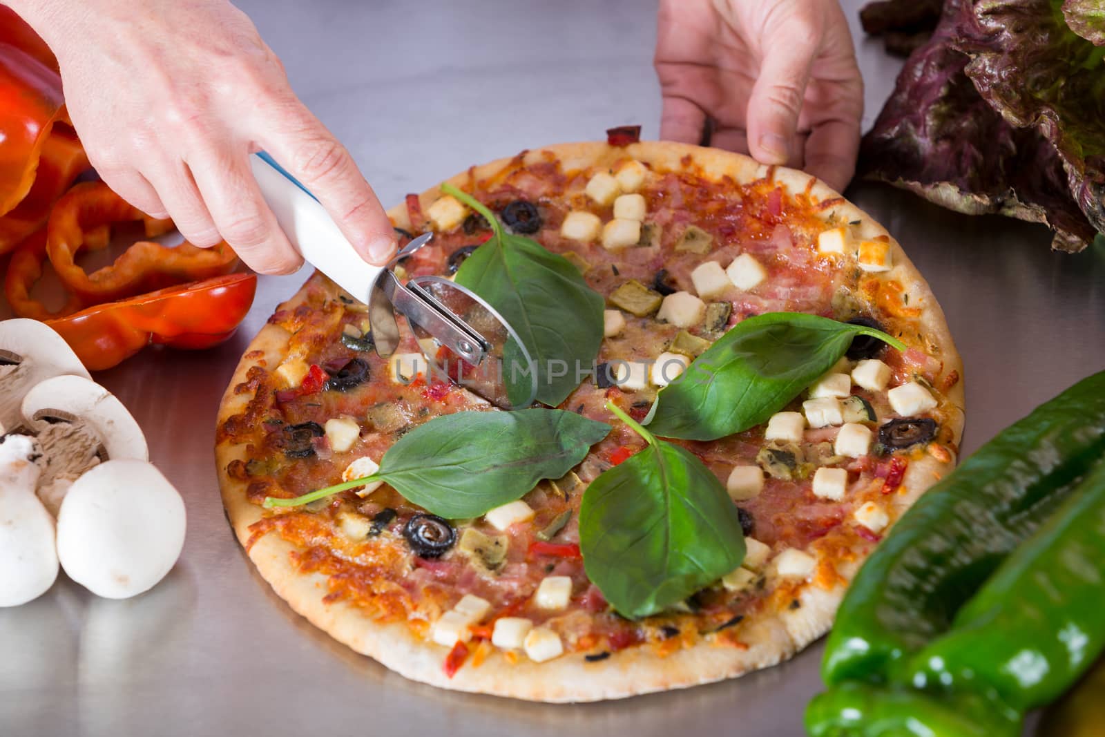 Cook cutting a Mediterranean pizza with vegetables and cheese