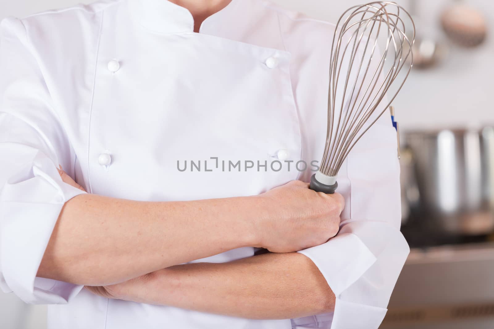 Chef in the kitchen with his arms crossed and with a whisk