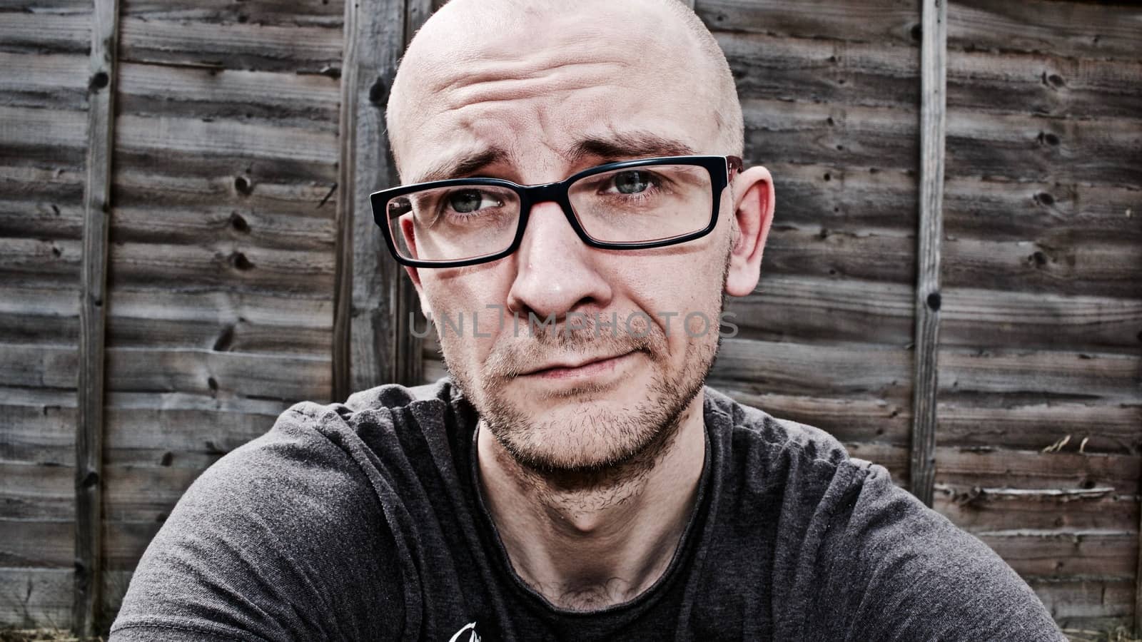 Young white man with glasses in garden near wooden fence.