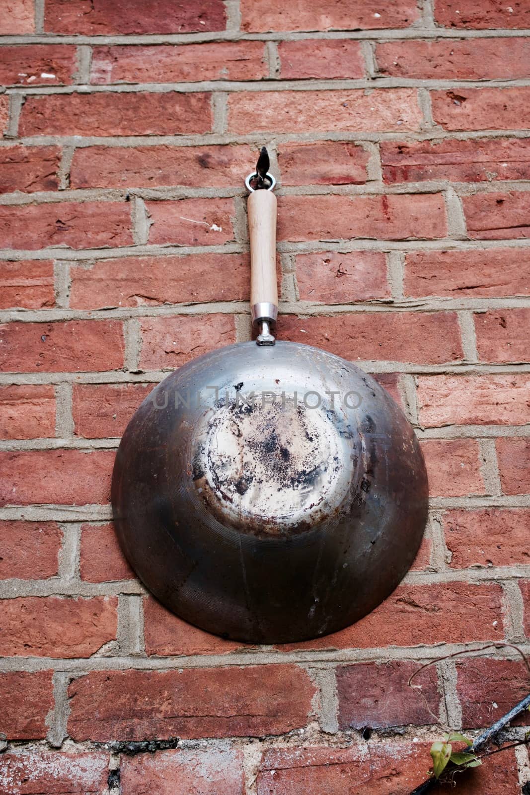 Big old and dirty pan on the brick wall in the garden. Abstract concept.