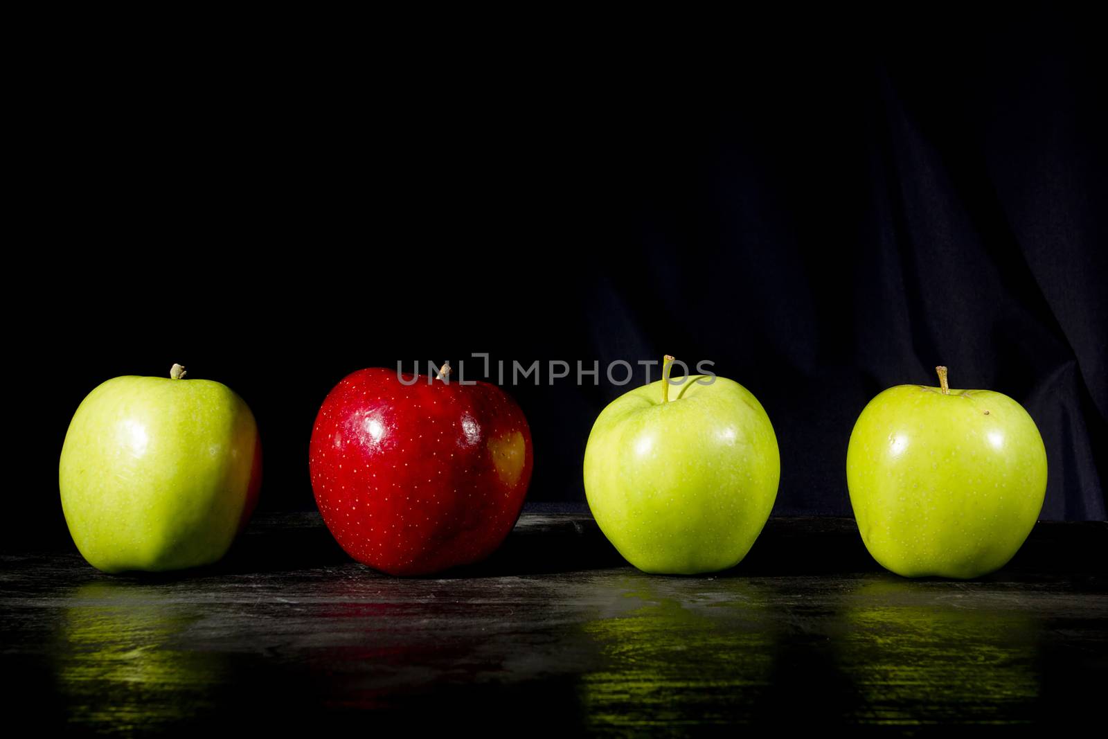 Red apple standing out in a row of green apples