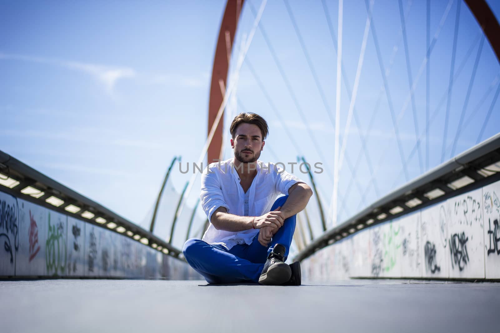 One handsome young man in urban setting in European city, sitting on the ground